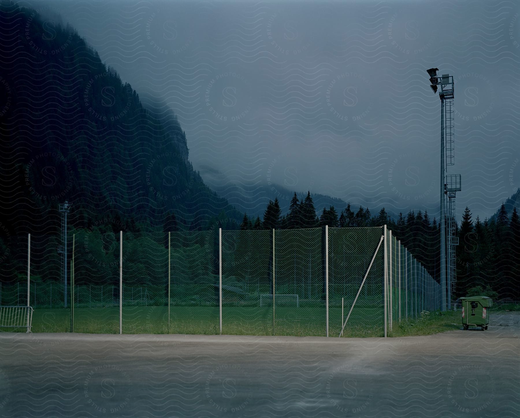 A land with a fence and a hill with a tree cage in the fence