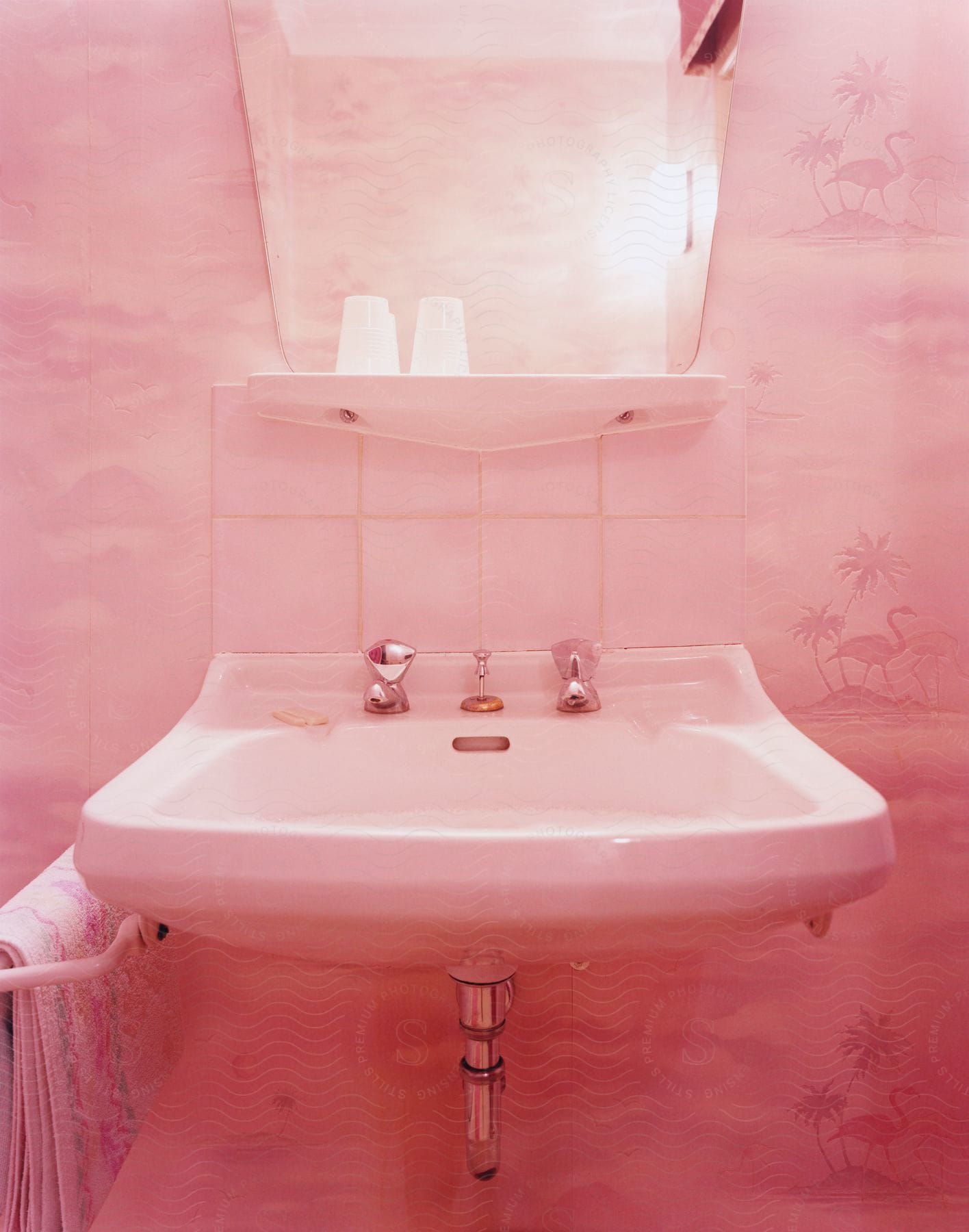 Pink bathroom interior with wallpaper featuring a sink mirror towel and tap