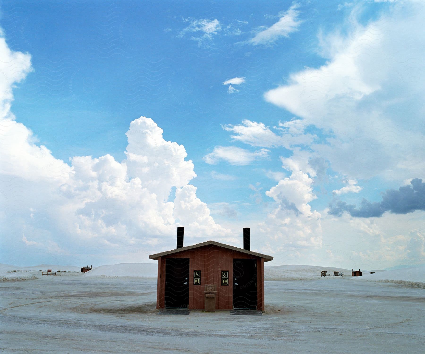 A wooden shed bathroom in a white sands desert under a light blue sky with fluffy clouds
