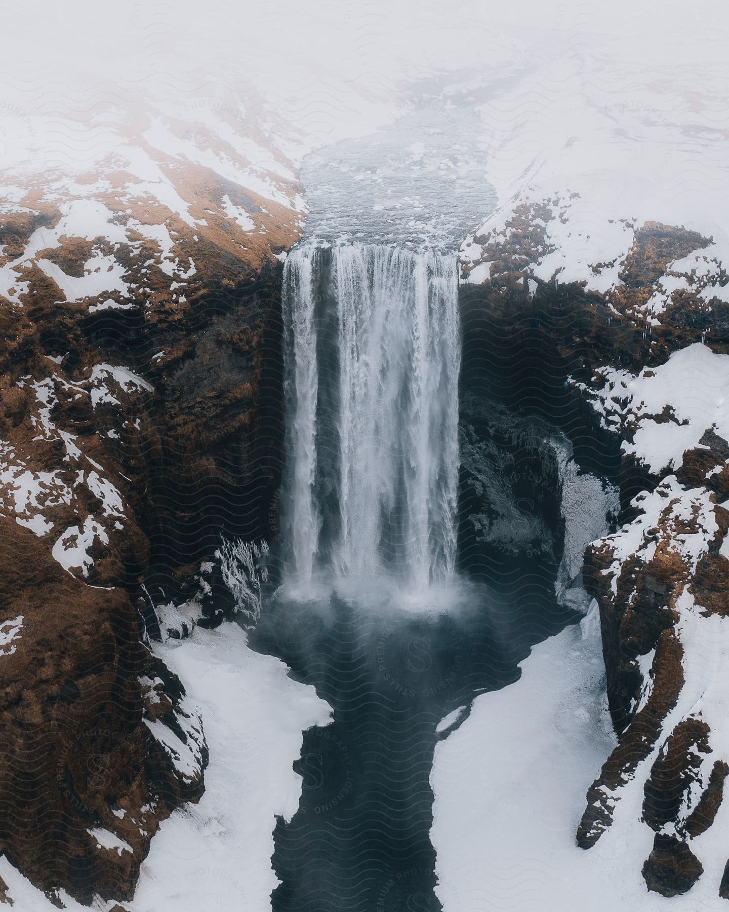 A winter waterfall with snowcovered ground flowing over a cliff into a river