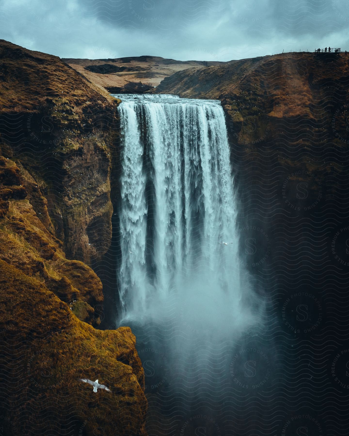 Waterfall on mountain with flying bird distant silhouettes of people