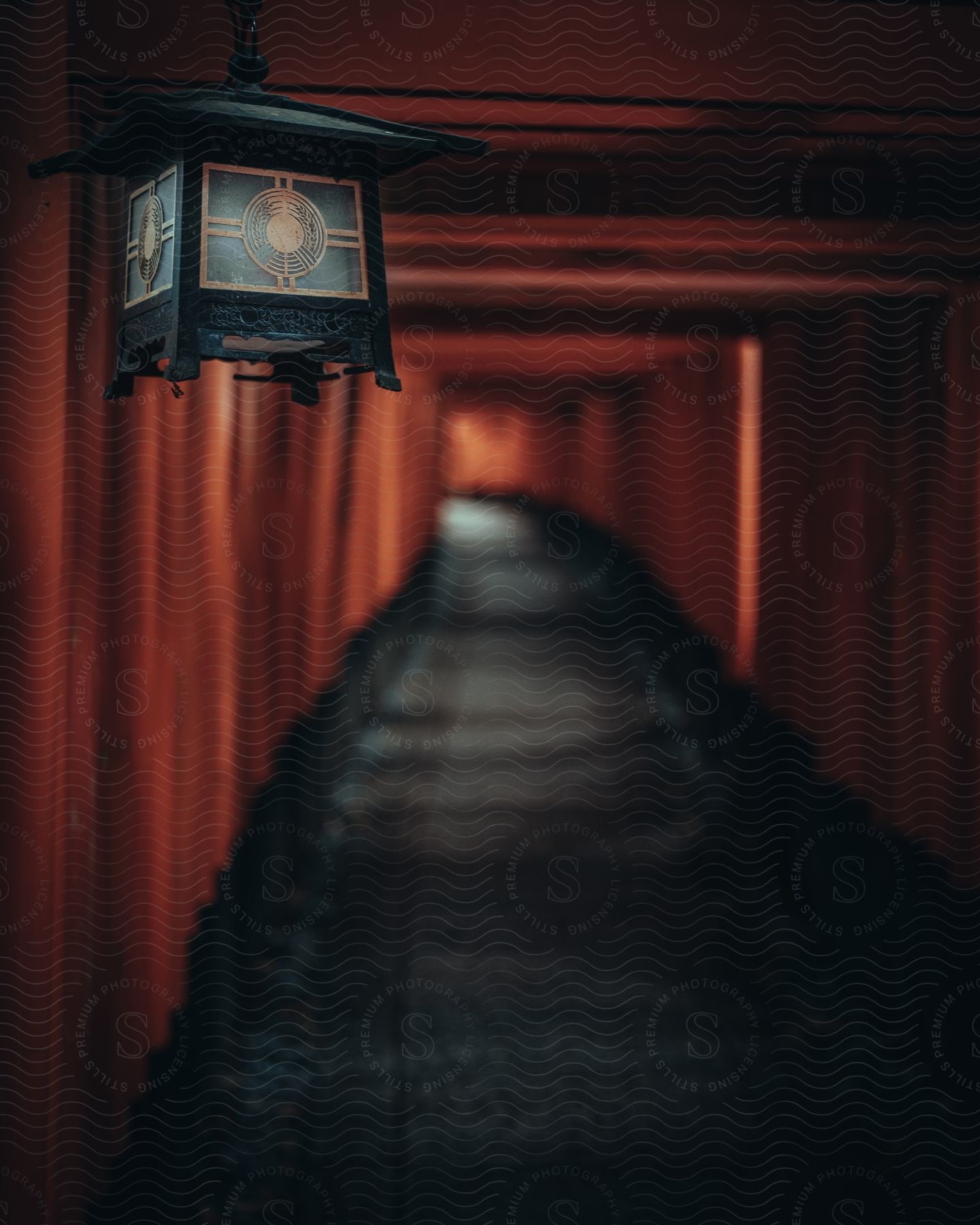 An antique asian lamp hangs at the entrance of a long wooden tunnel