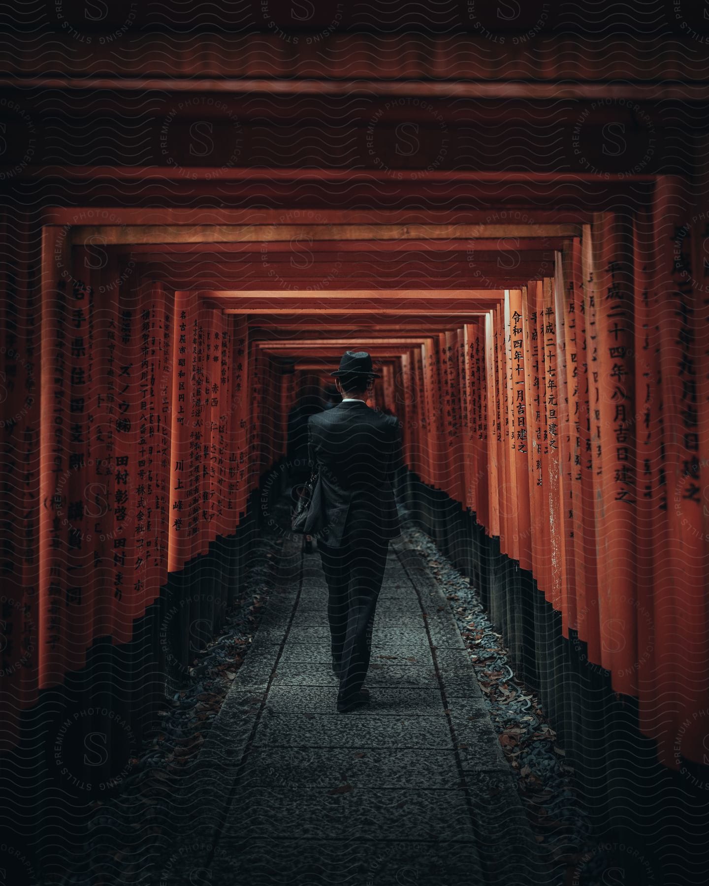 A man in a suit and hat walks down a corridor with columns that have words etched on them