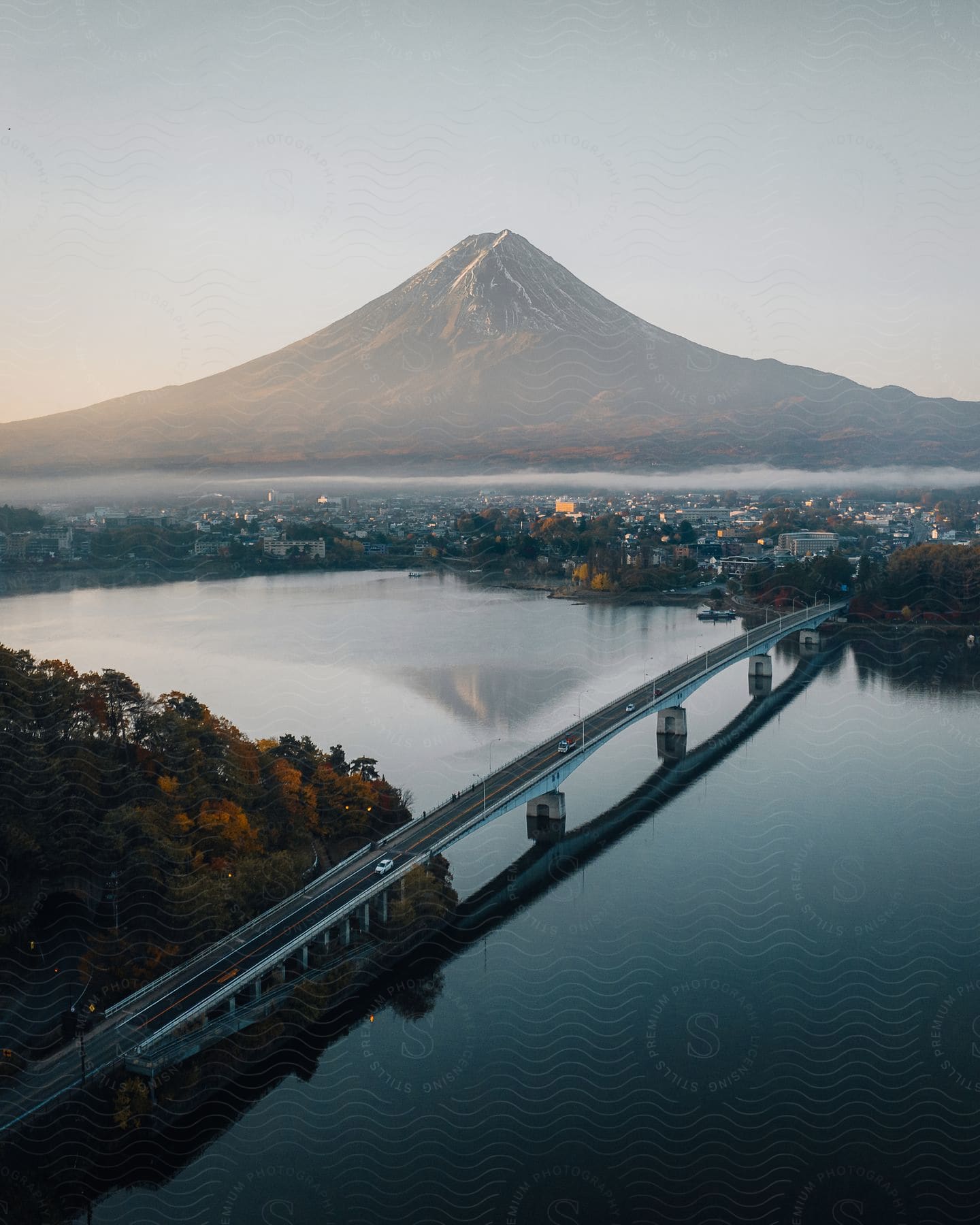 An aerial view of a bridge over water leading to a rural village with a volcano in the distance