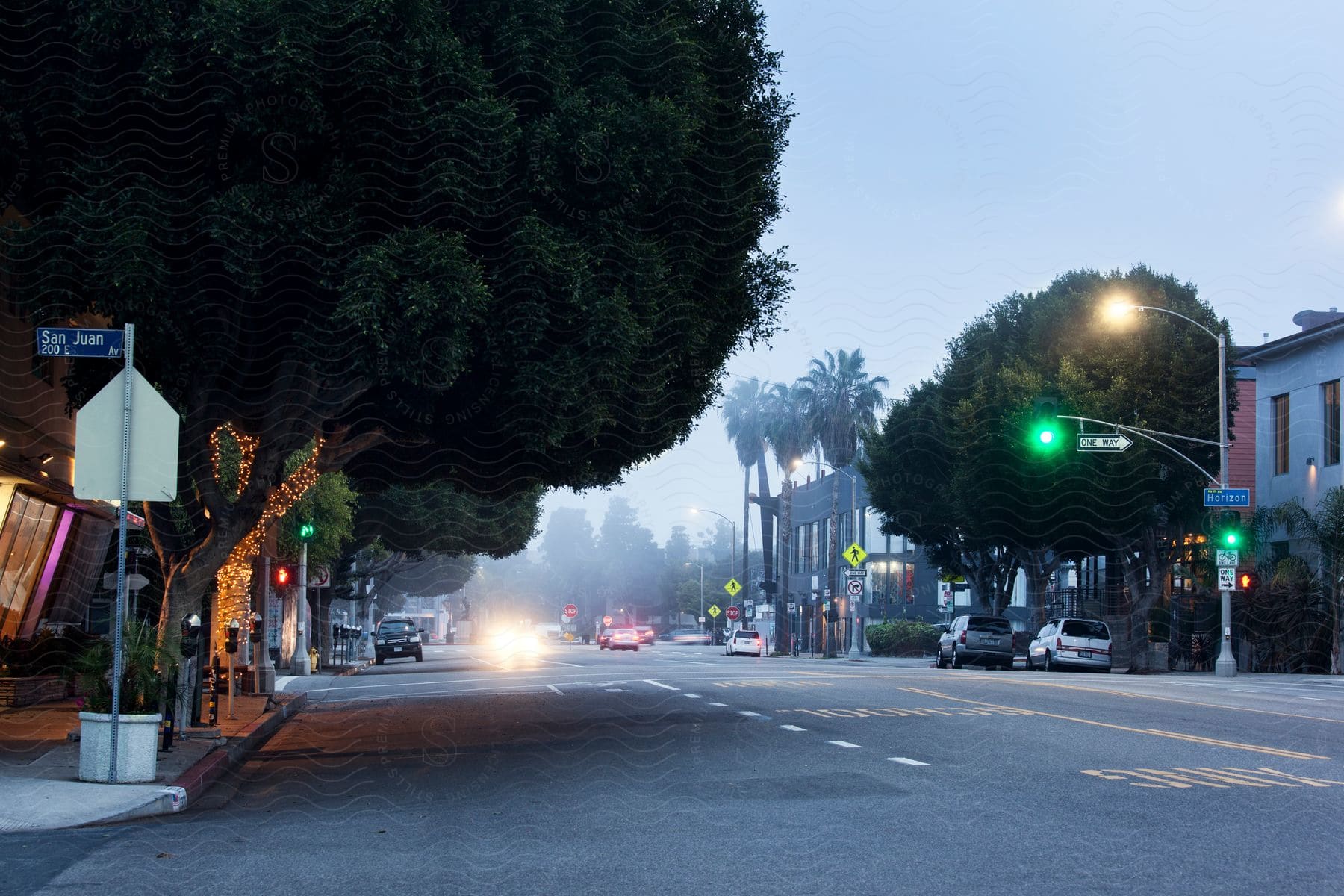 A city street at dusk with street lights traffic lights and cars