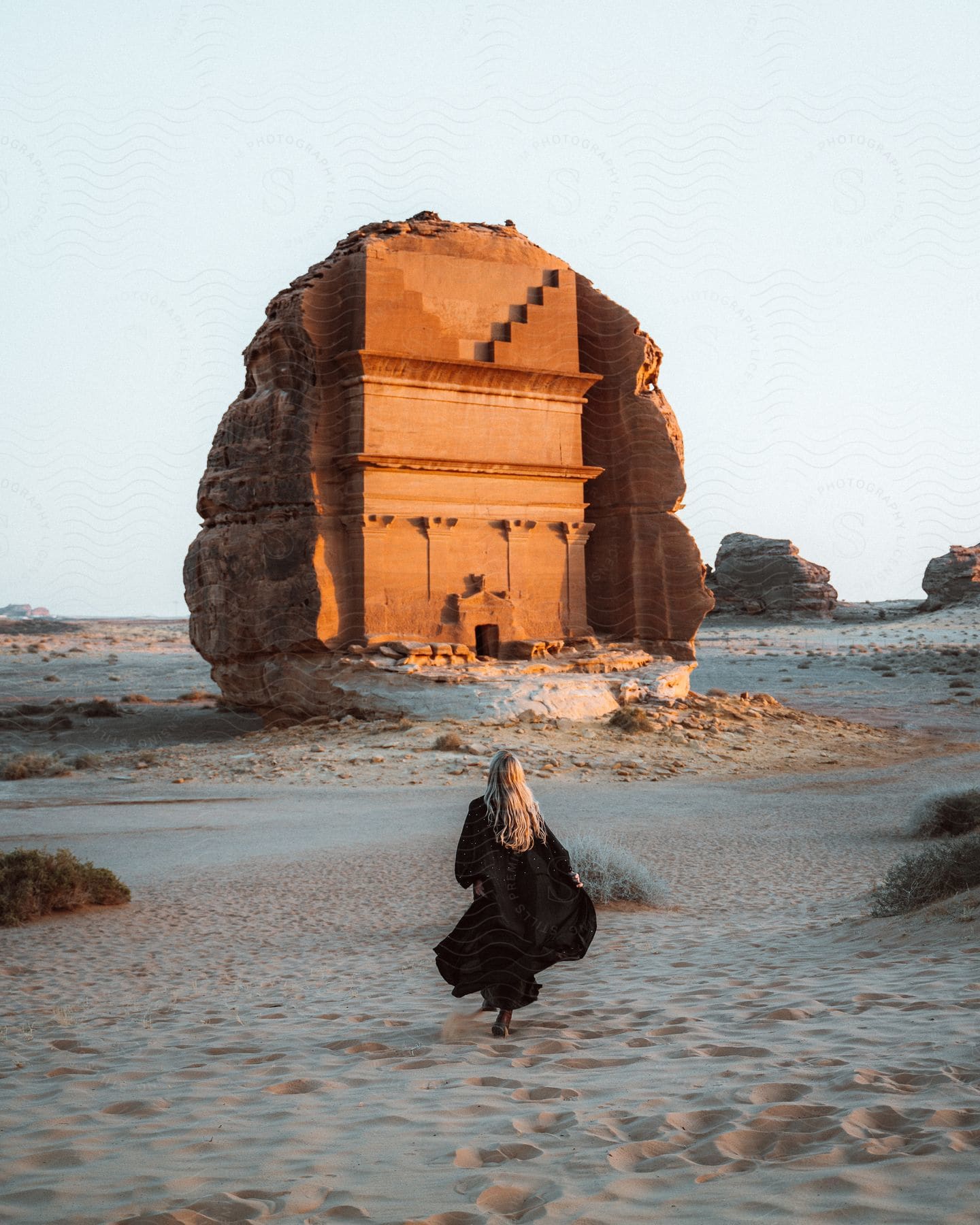 Stock photo of blonde woman with black dress walks up to tomb of lihyan son of kuza in the desert in saudi arabia