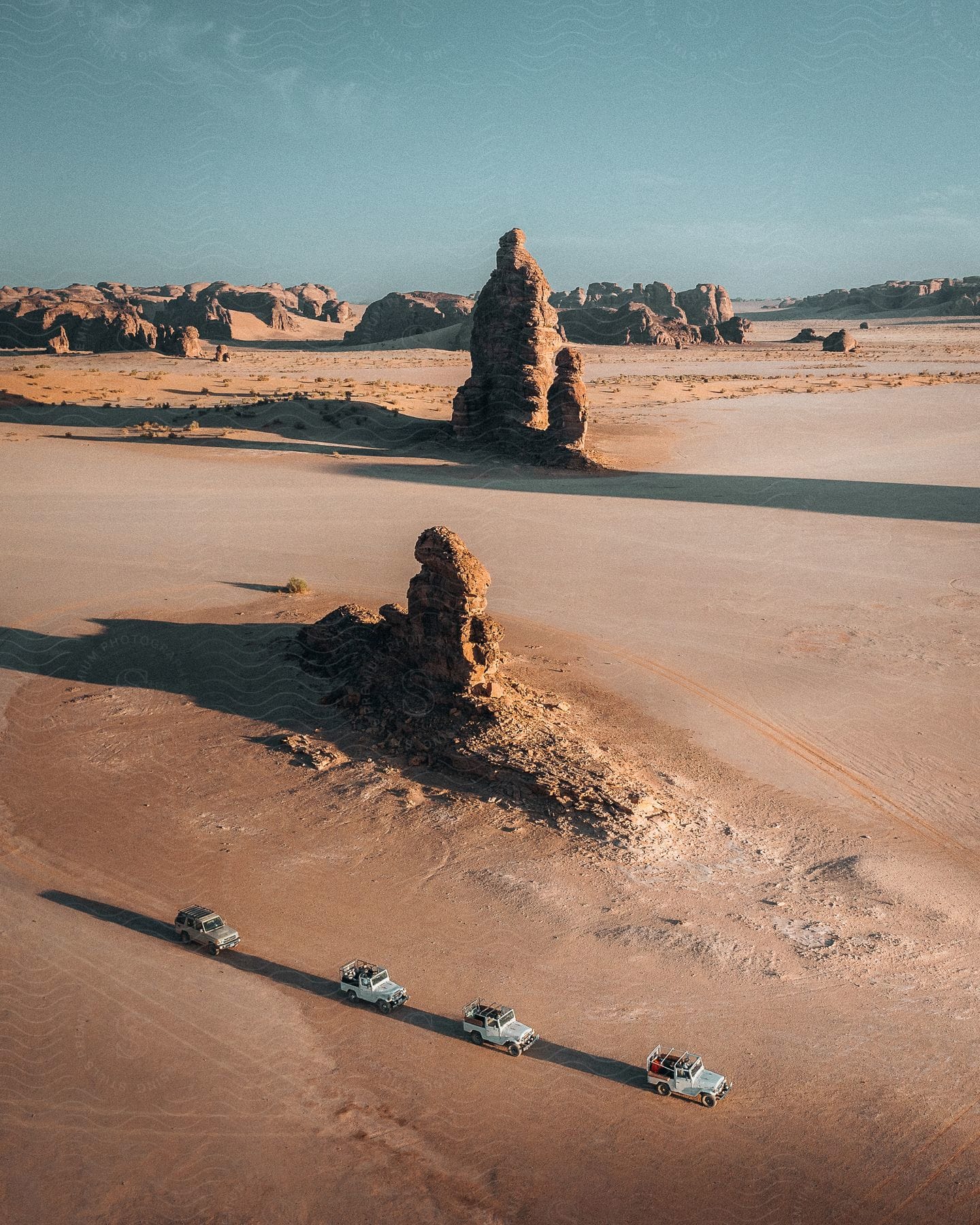 In the desert four cars drive through hilly terrain kicking up dust