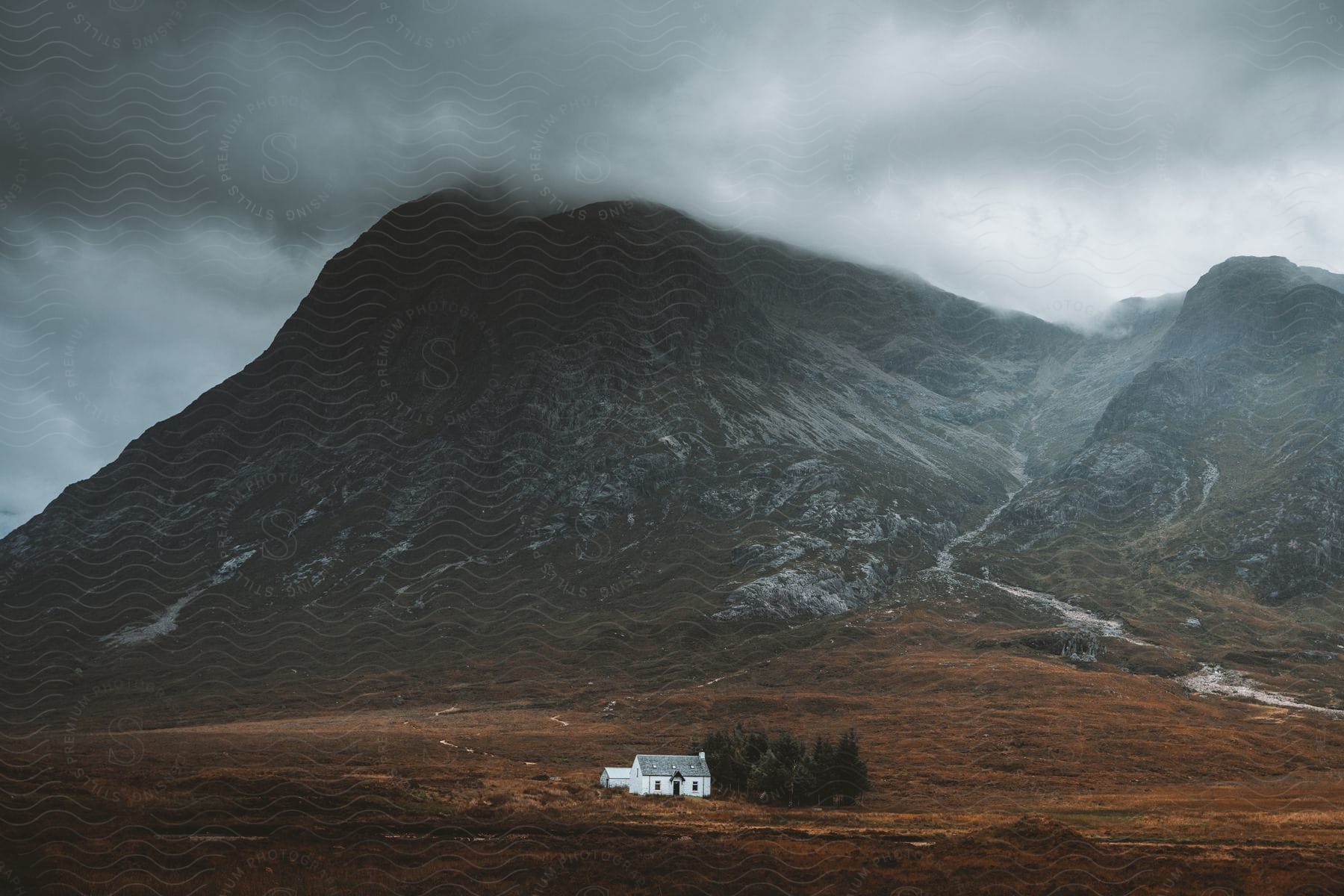 Wide landscape shot of a white house next to a mountain range in scotland