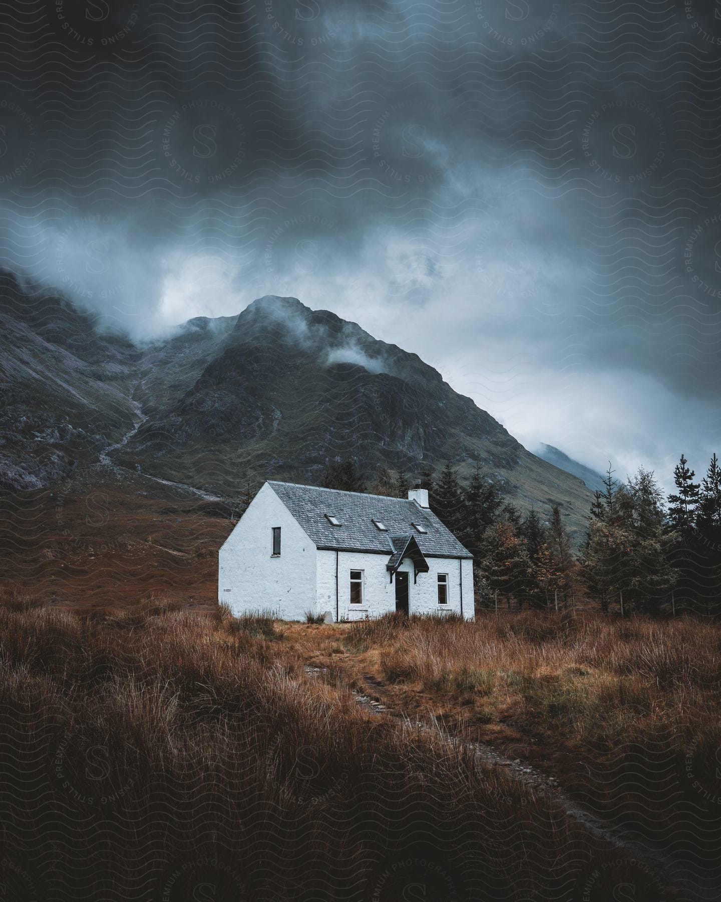 A white house on a mountainside surrounded by trees under a cloudy sky