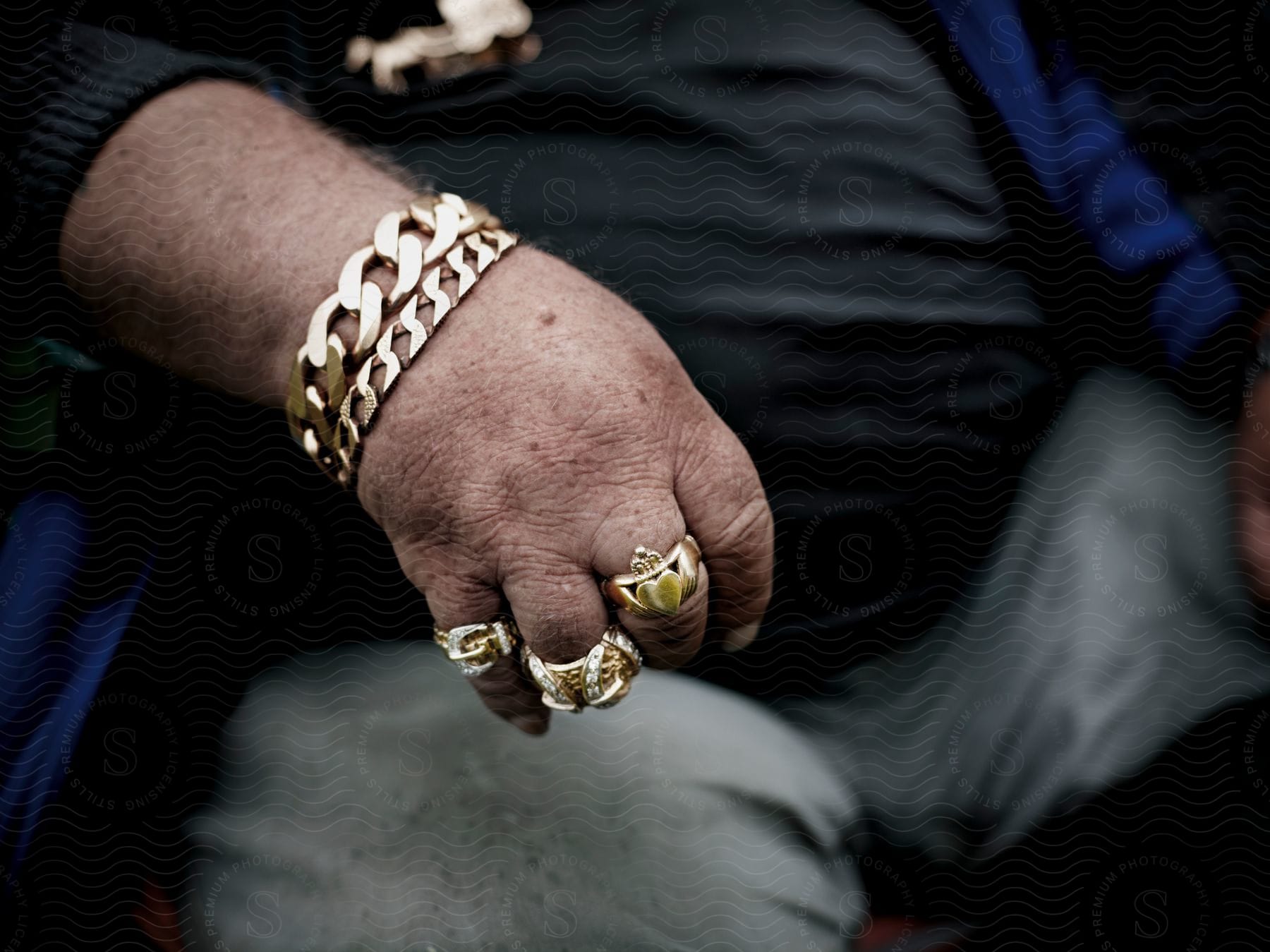 A mans hand holding jewelry including three rings on his fingers