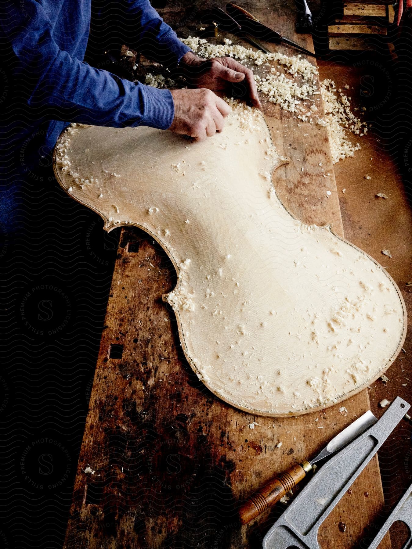 A luthier carving wood and handcrafting the body of a cello on a work bench