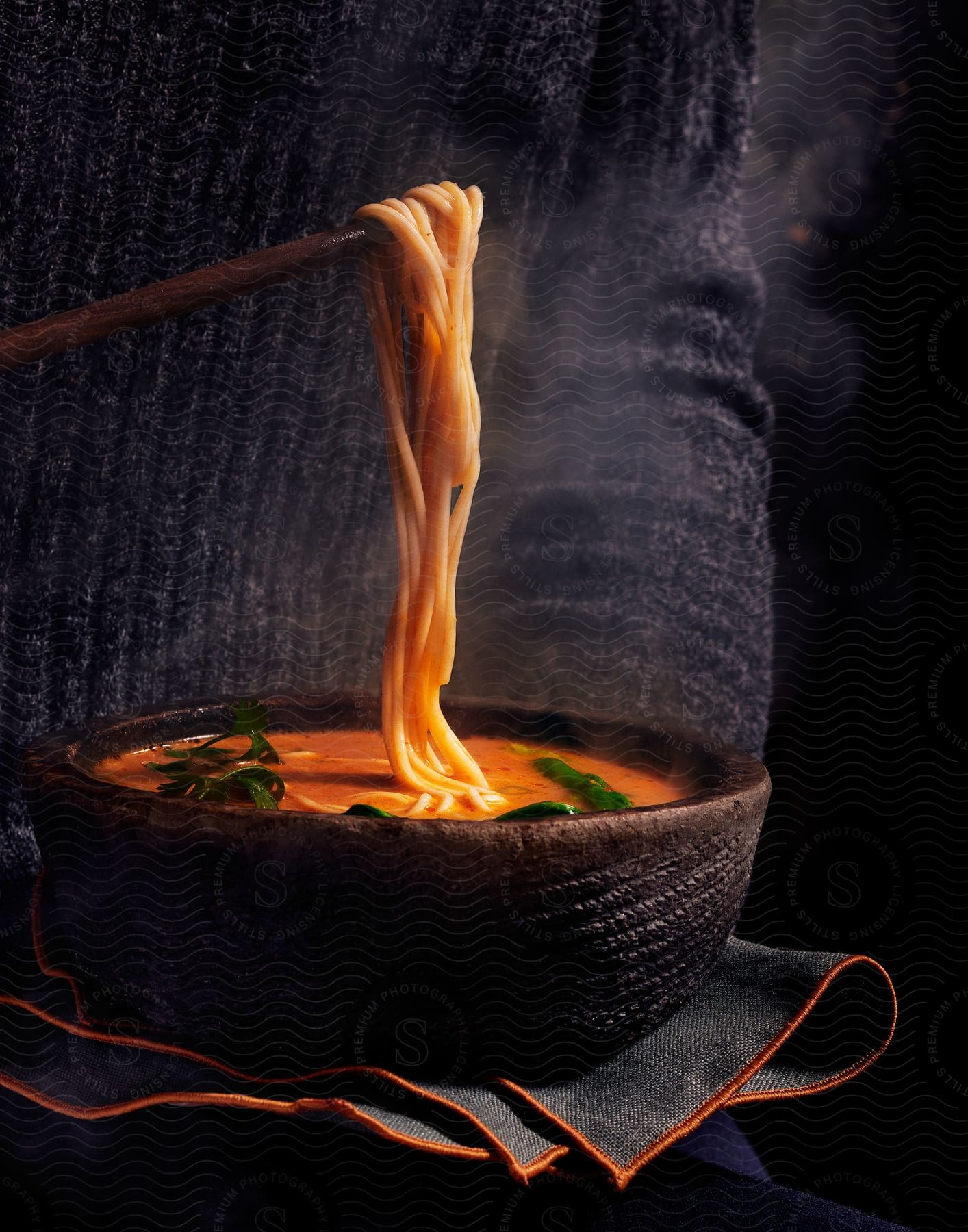 A bowl of steaming soup with noodles being held by a chopstick