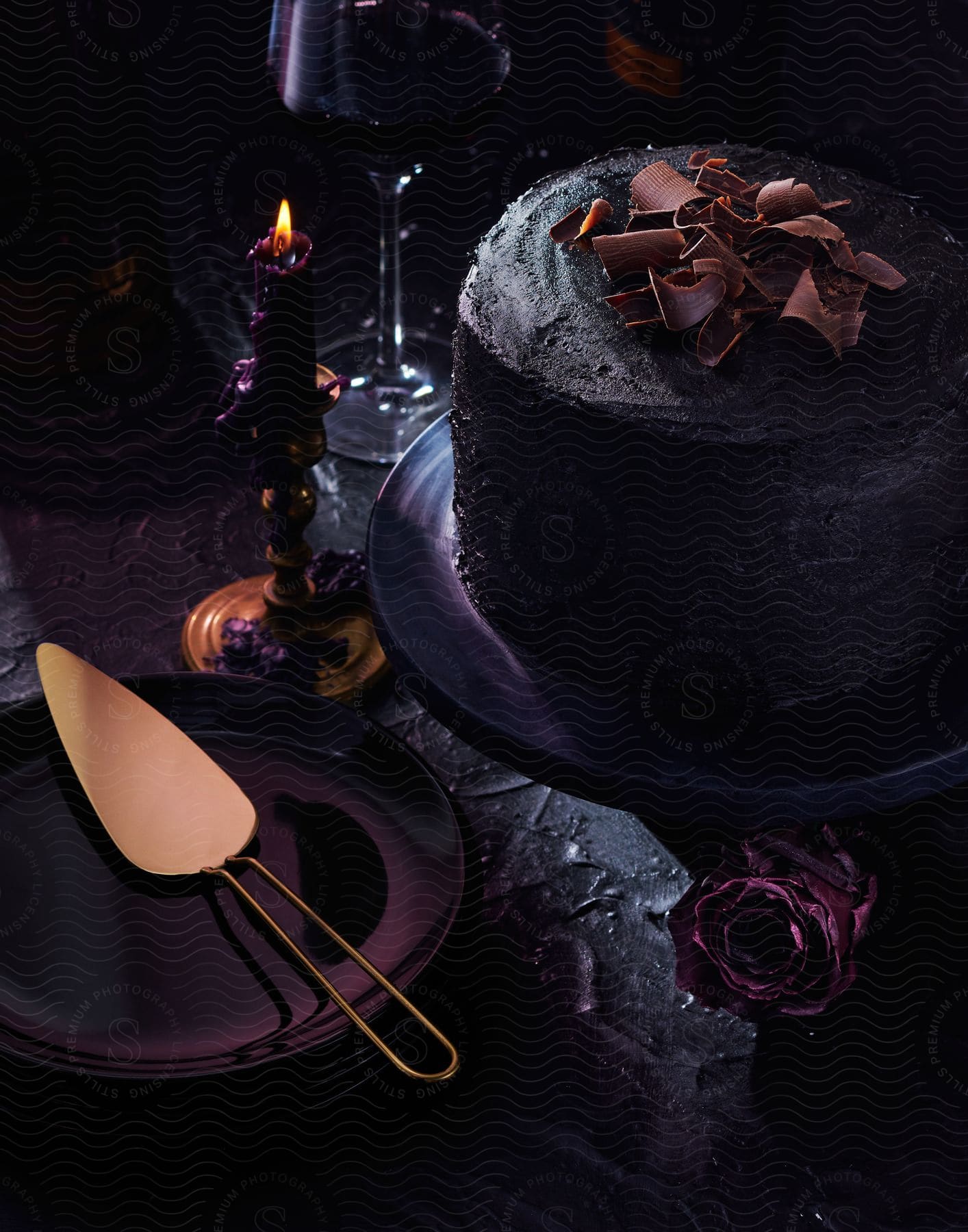 A gothicstyle chocolate cake with a darkcolored rose and candle displayed on a plate