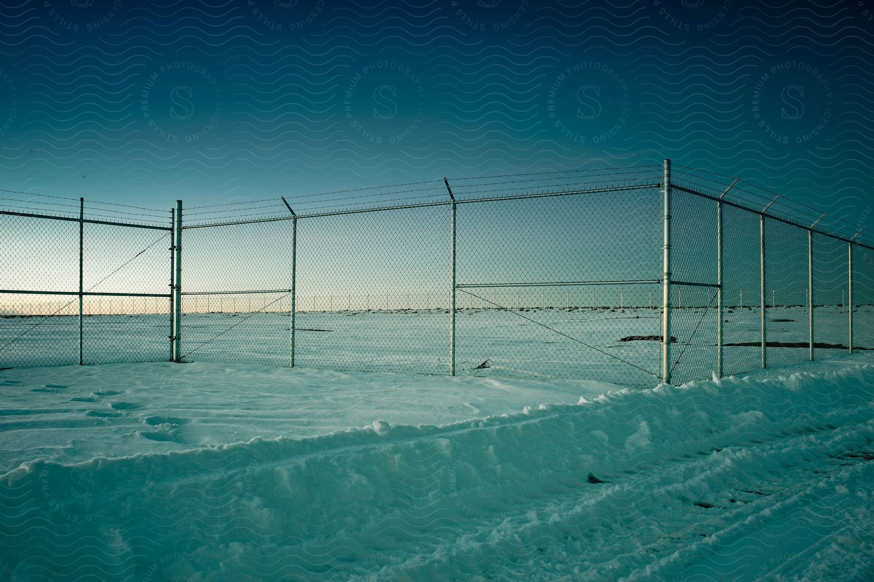 A snowy field is blocked off by a chainlinked fence