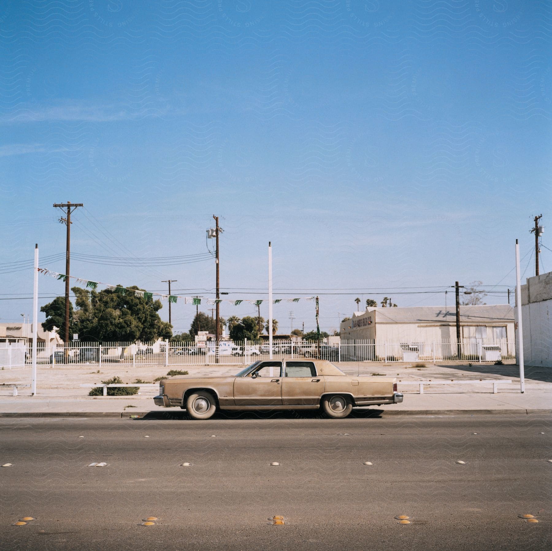 A street with a fence and an old car parked close to the fence