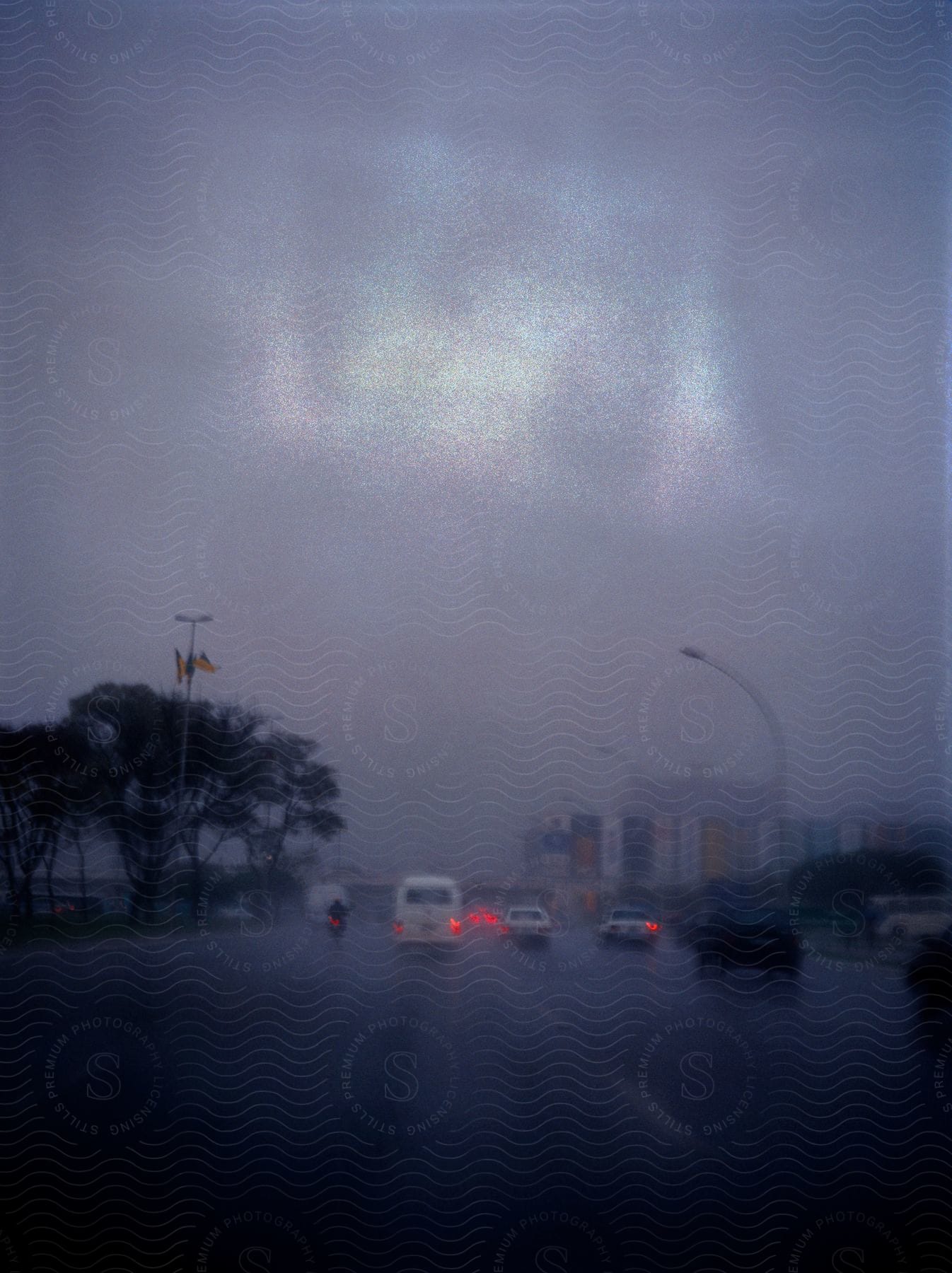 Traffic moves along highway on rainy day as sun tries to shine through heavy clouds