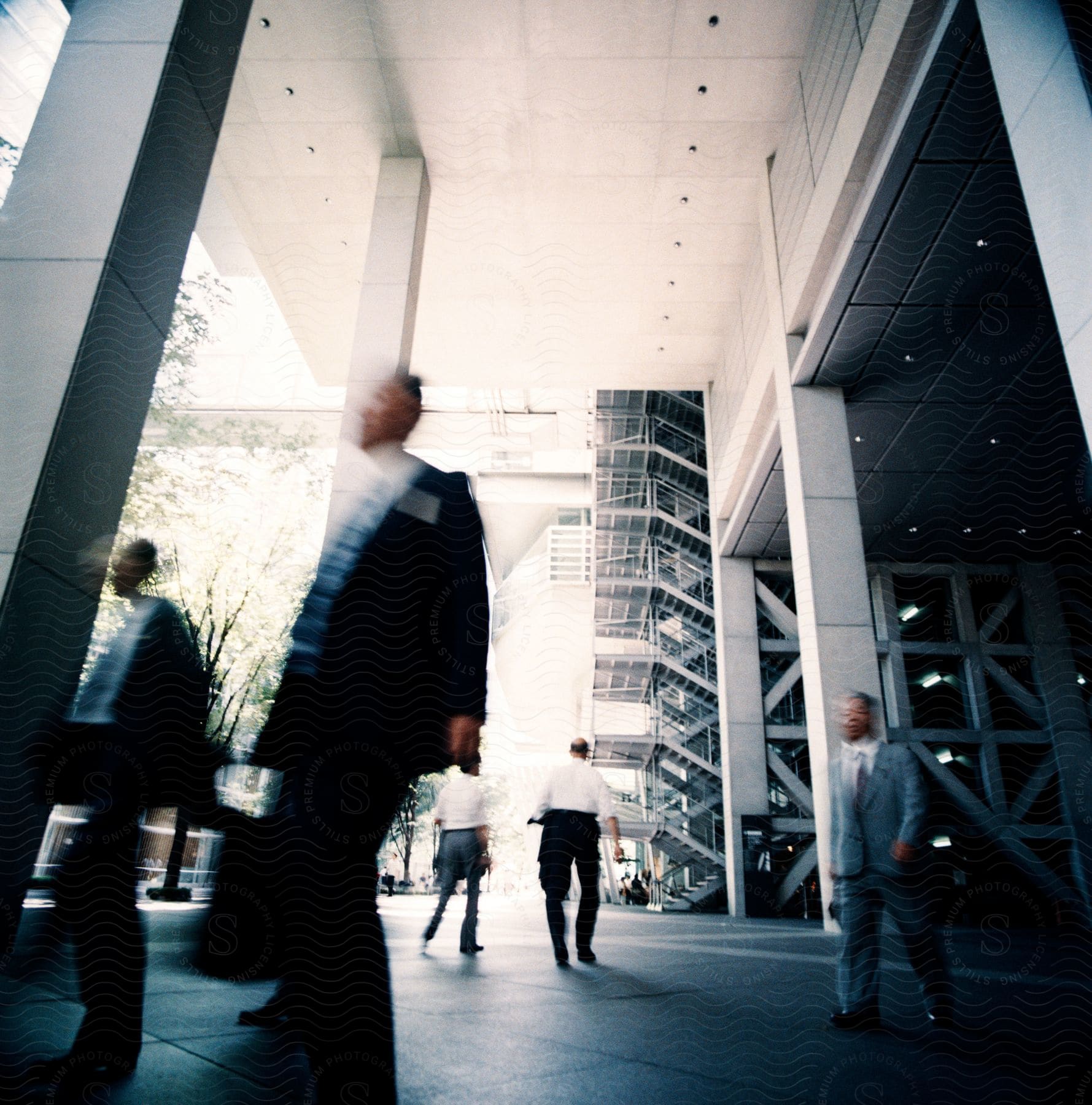 Businessmen walking in blurred motion under a tall building with columns and stairs on a sunny day