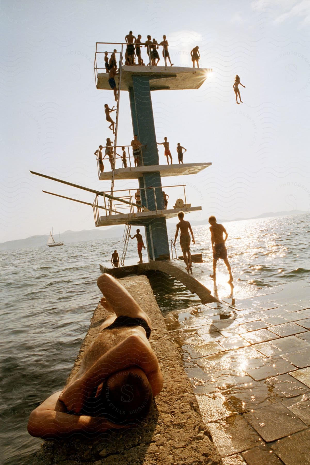 People sunbathe and wait to dive off a steep diving board in the ocean