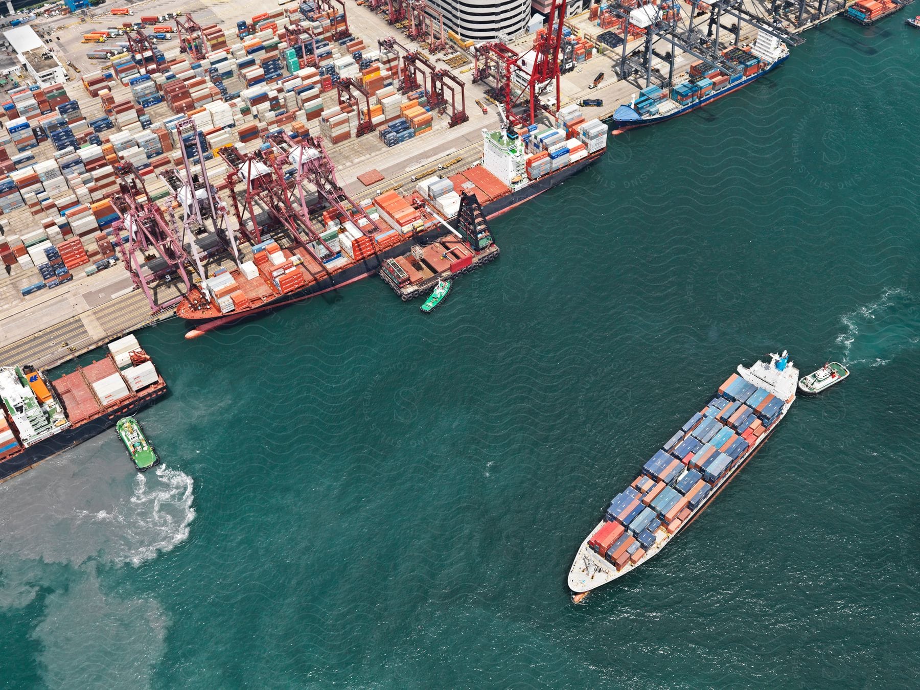 An aerial perspective of a cargo ship with shipping containers entering a port where cranes are unloading the containers