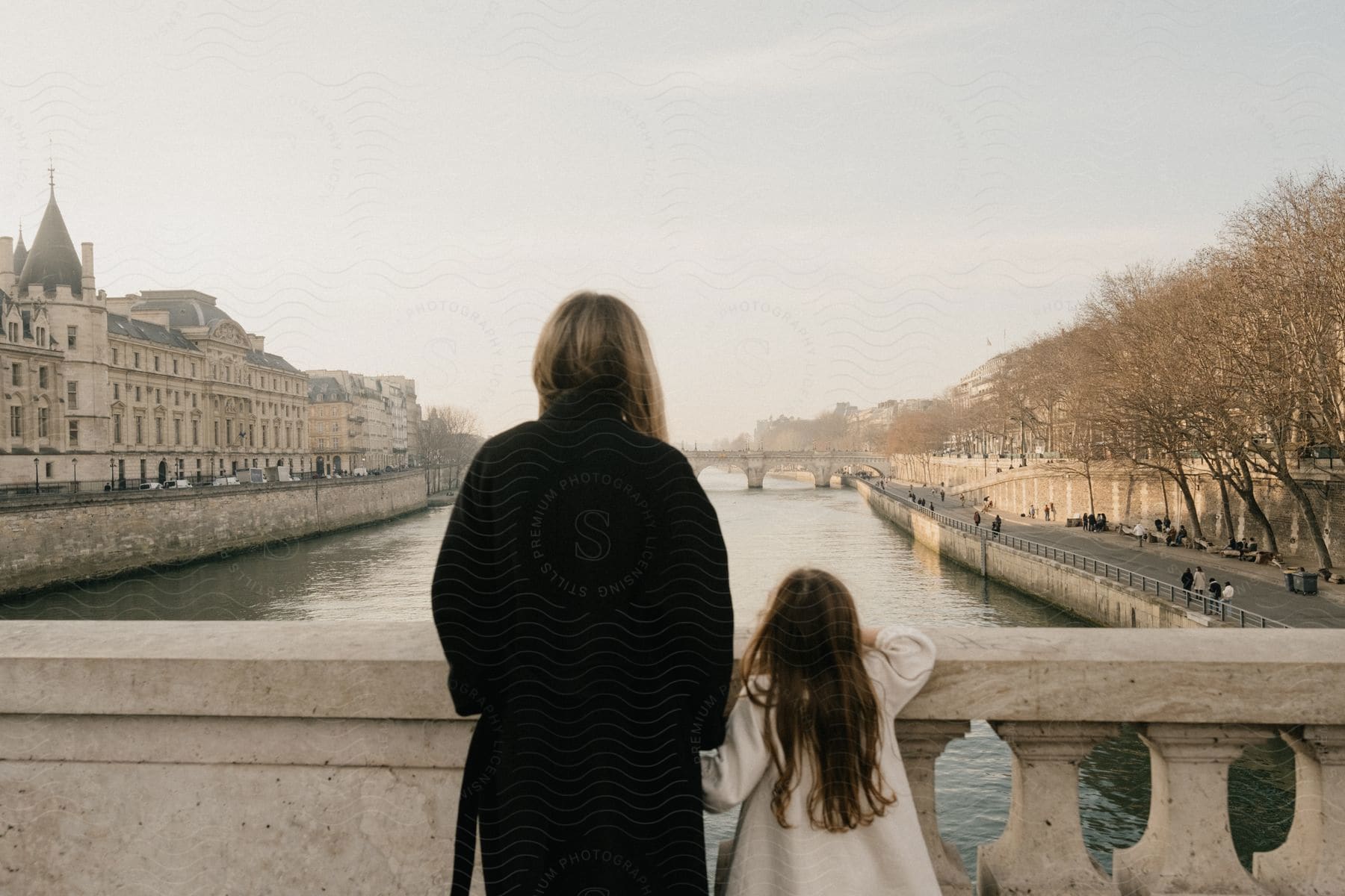 A mother and daughter stand on a bridge overlooking a canal in paris