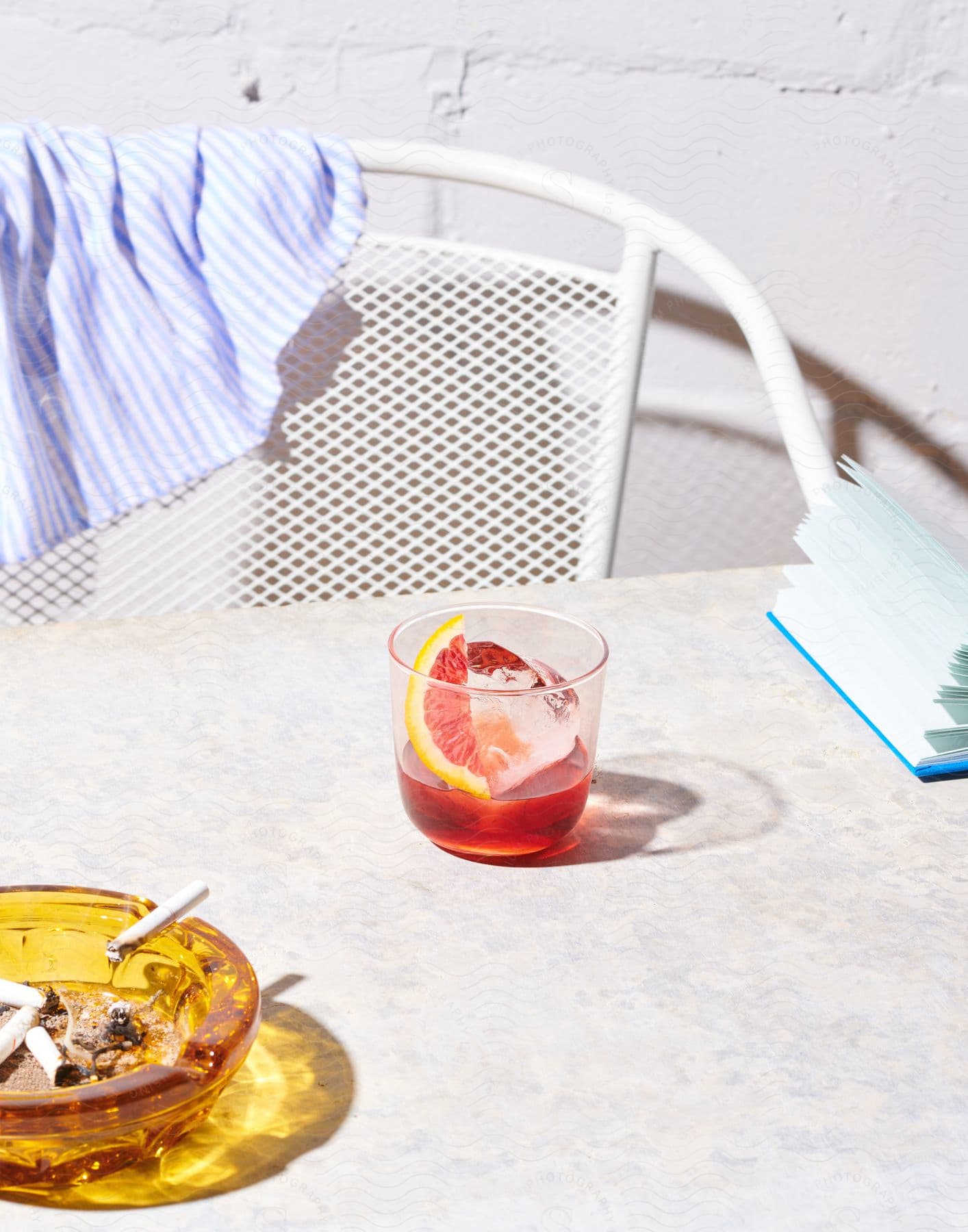 Stock photo of red drink with lemon slice and ice on white table with ashtray and cigarette