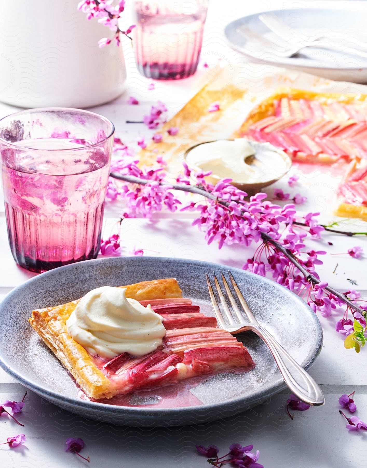 A slice of pie with cream water and purple flowers on a table