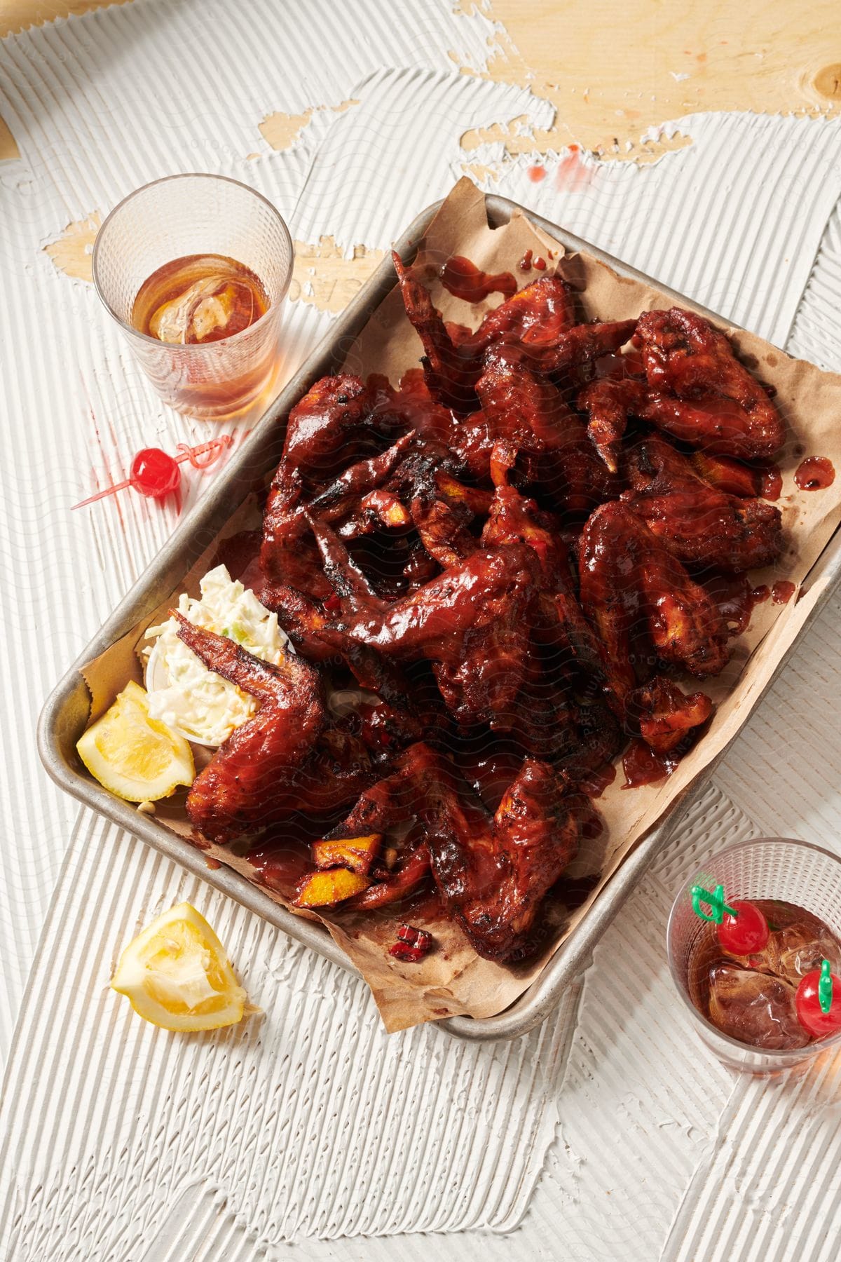 A plate of chicken legs surrounded by drinks cherries and lemon wedges