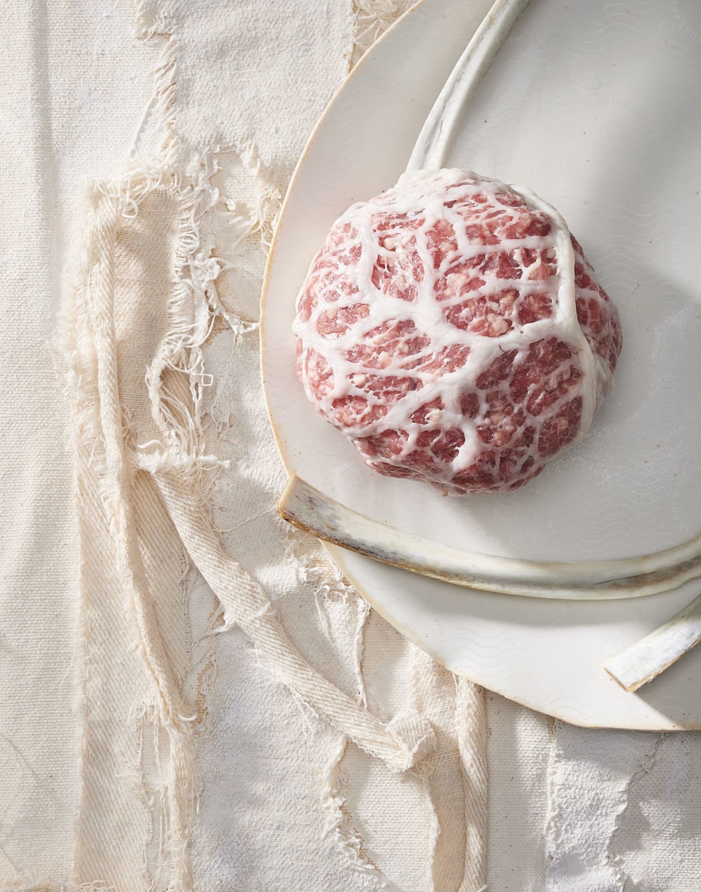 A patty of ground beef with streaks of fat on a white plate