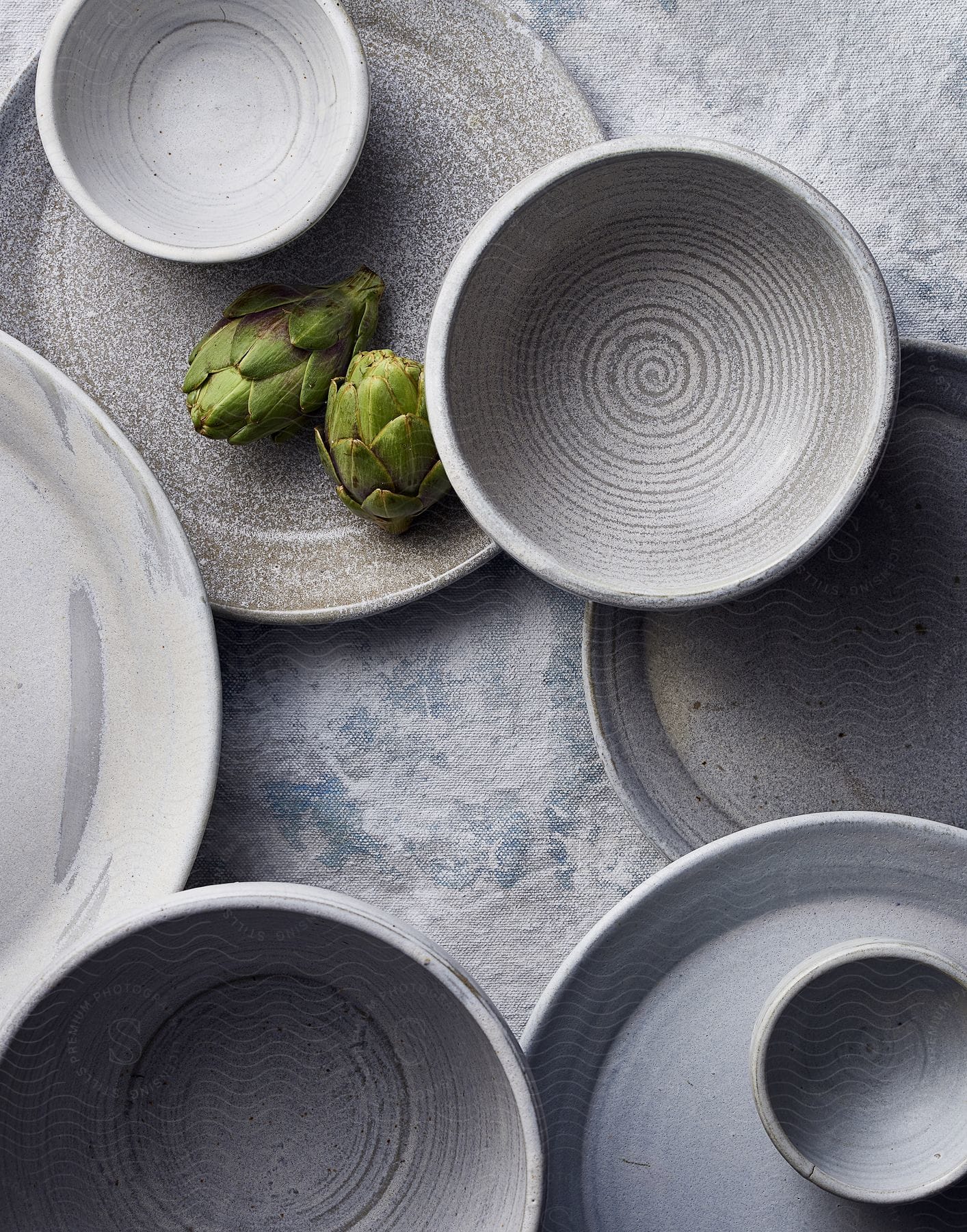 Two artichokes on a plate surrounded by gray tableware wear on a table