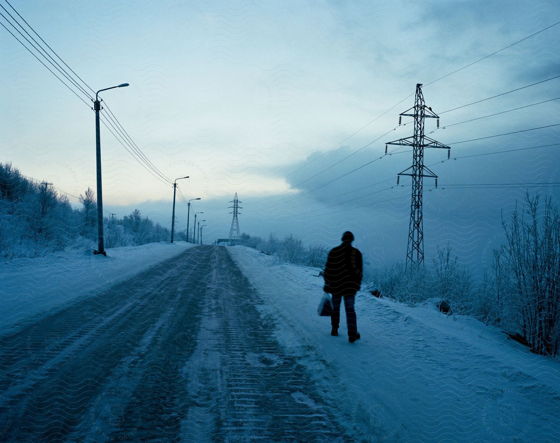 A man wearing a black hat coat and pants is walking down a snowy road