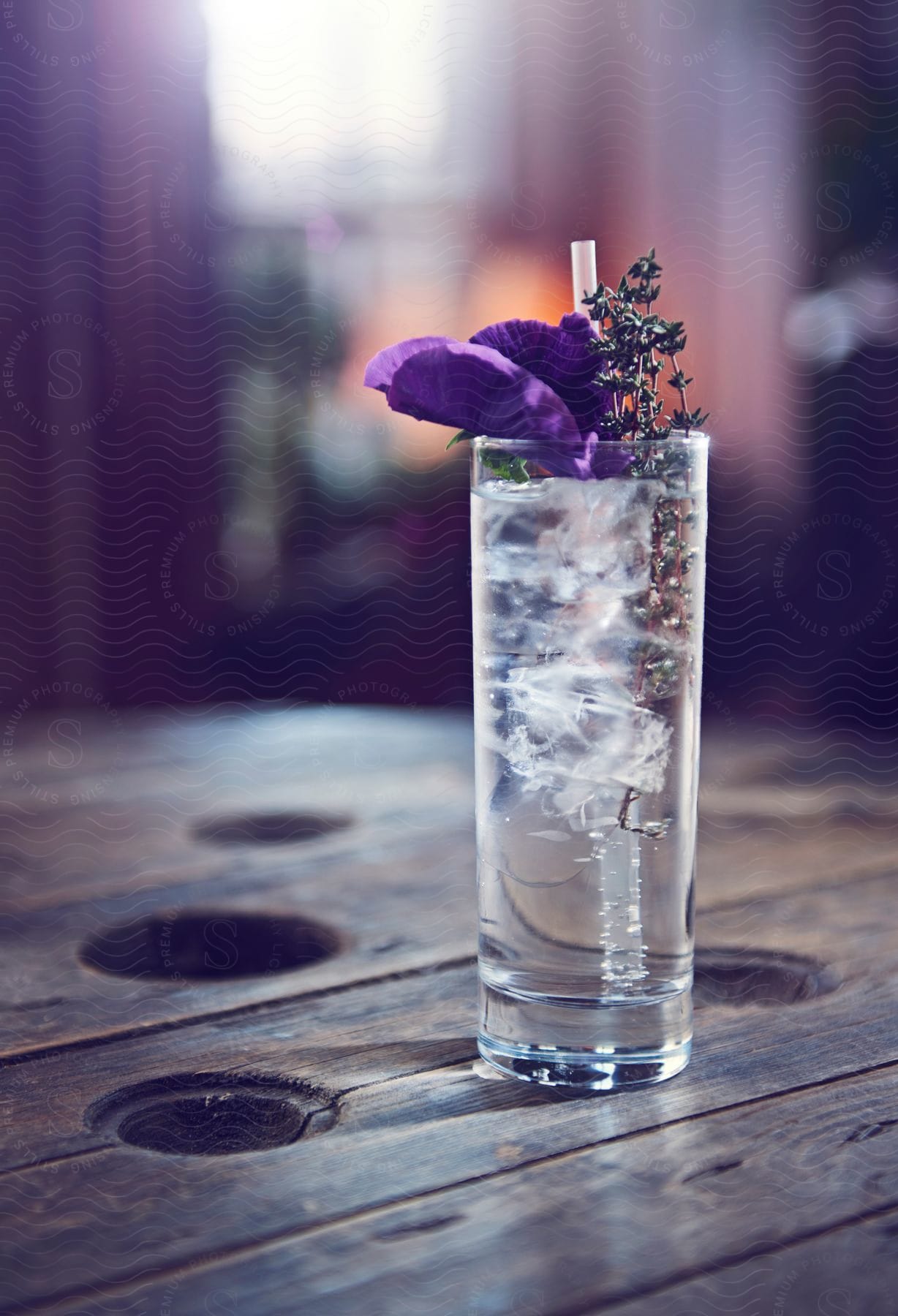 A glass of water with a purple flower and mint twig sits on a wooden table