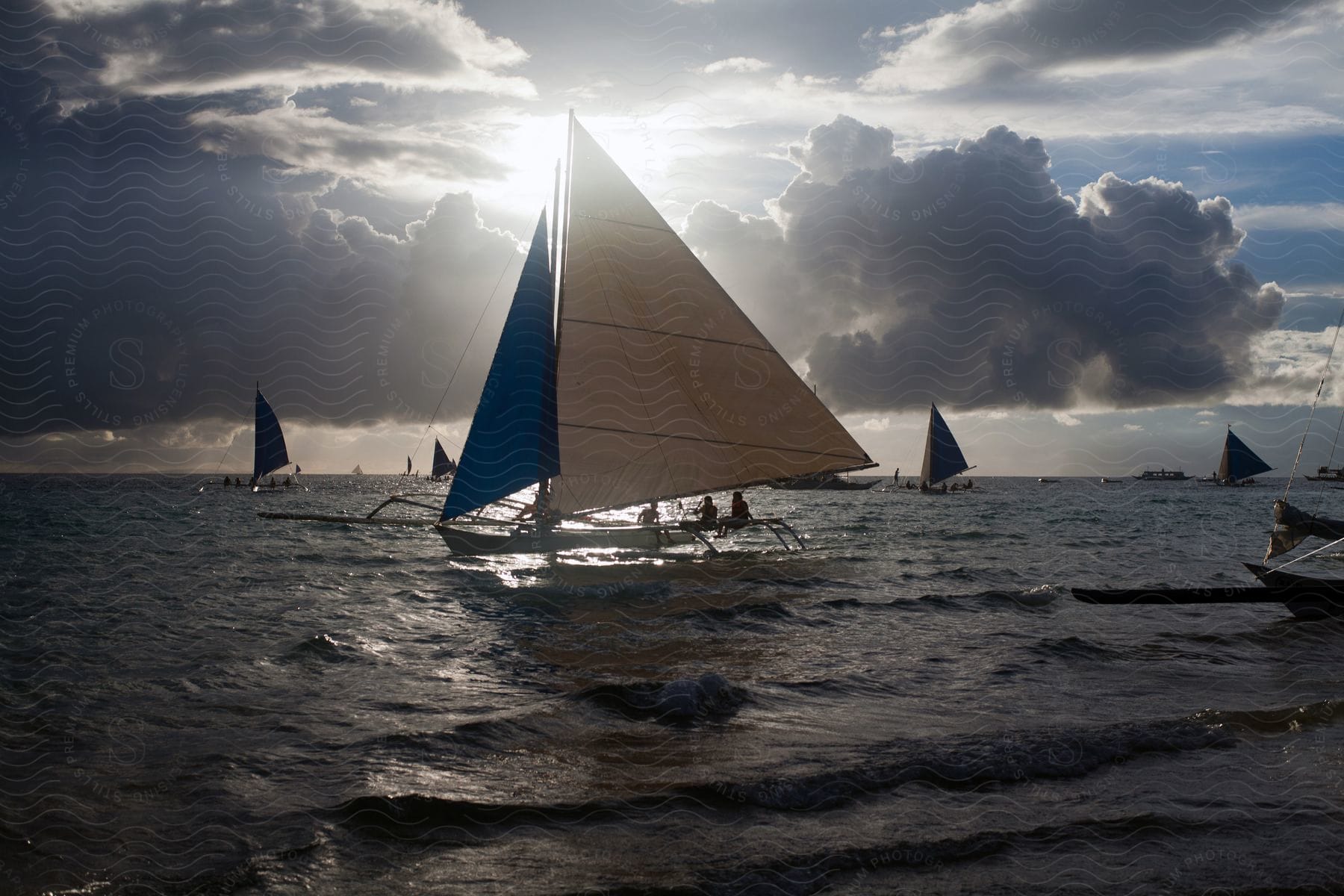Several sailboats in the ocean on a cloudy day at sunset