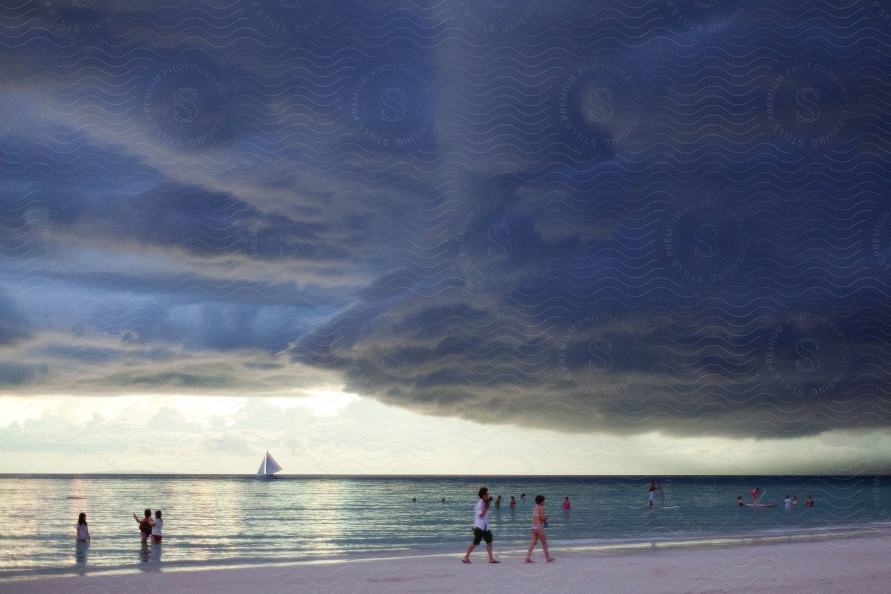 People swim in the ocean and walk on the beach under storm clouds