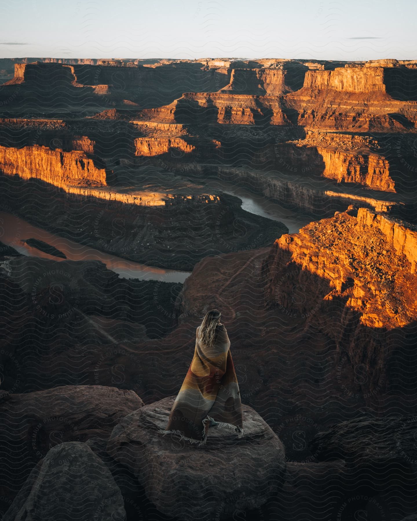 Person wearing poncho standing on high ground next to dead horse point looking at the landscape in utah