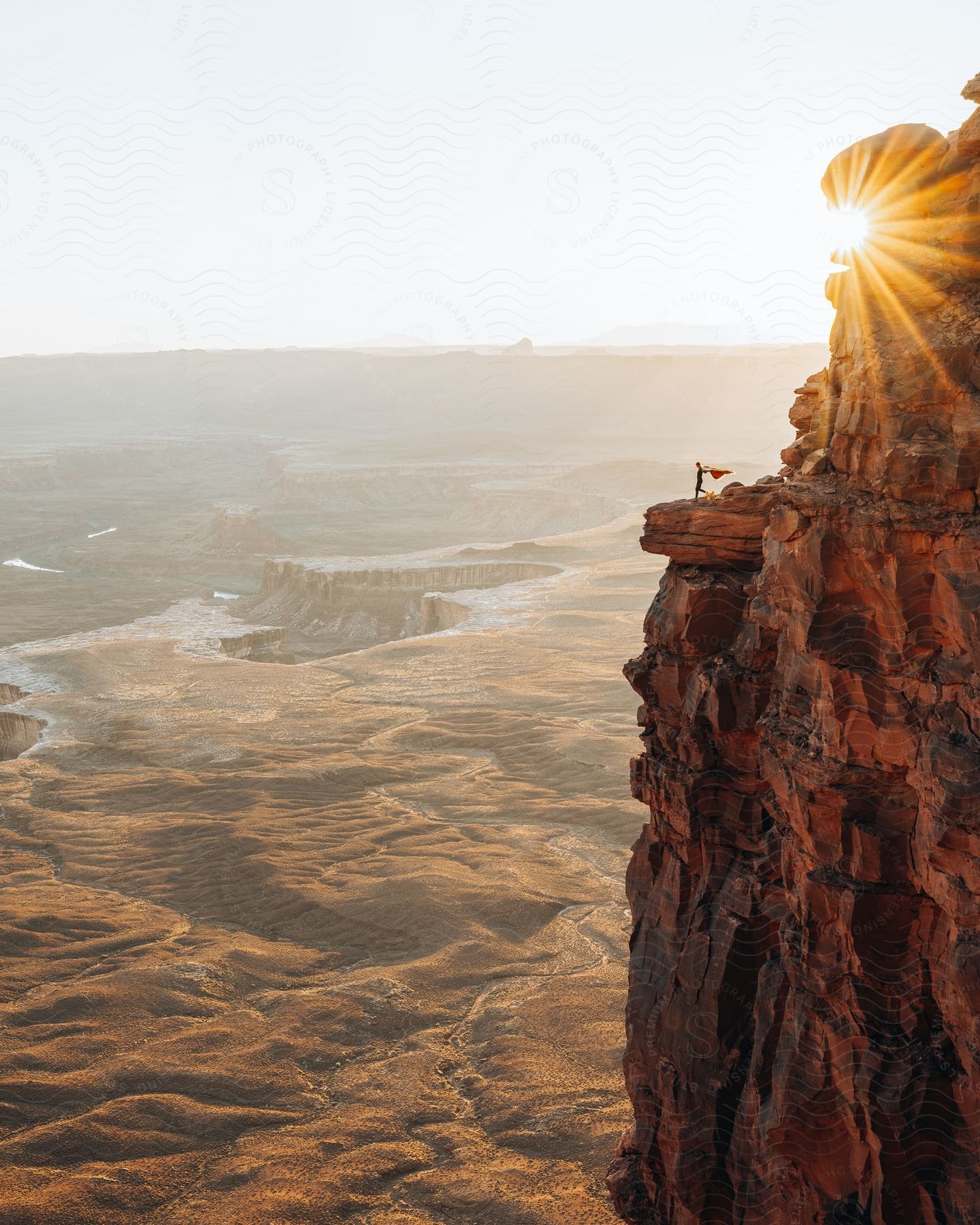 A person standing on a cliff face at sunset looking out over a canyon