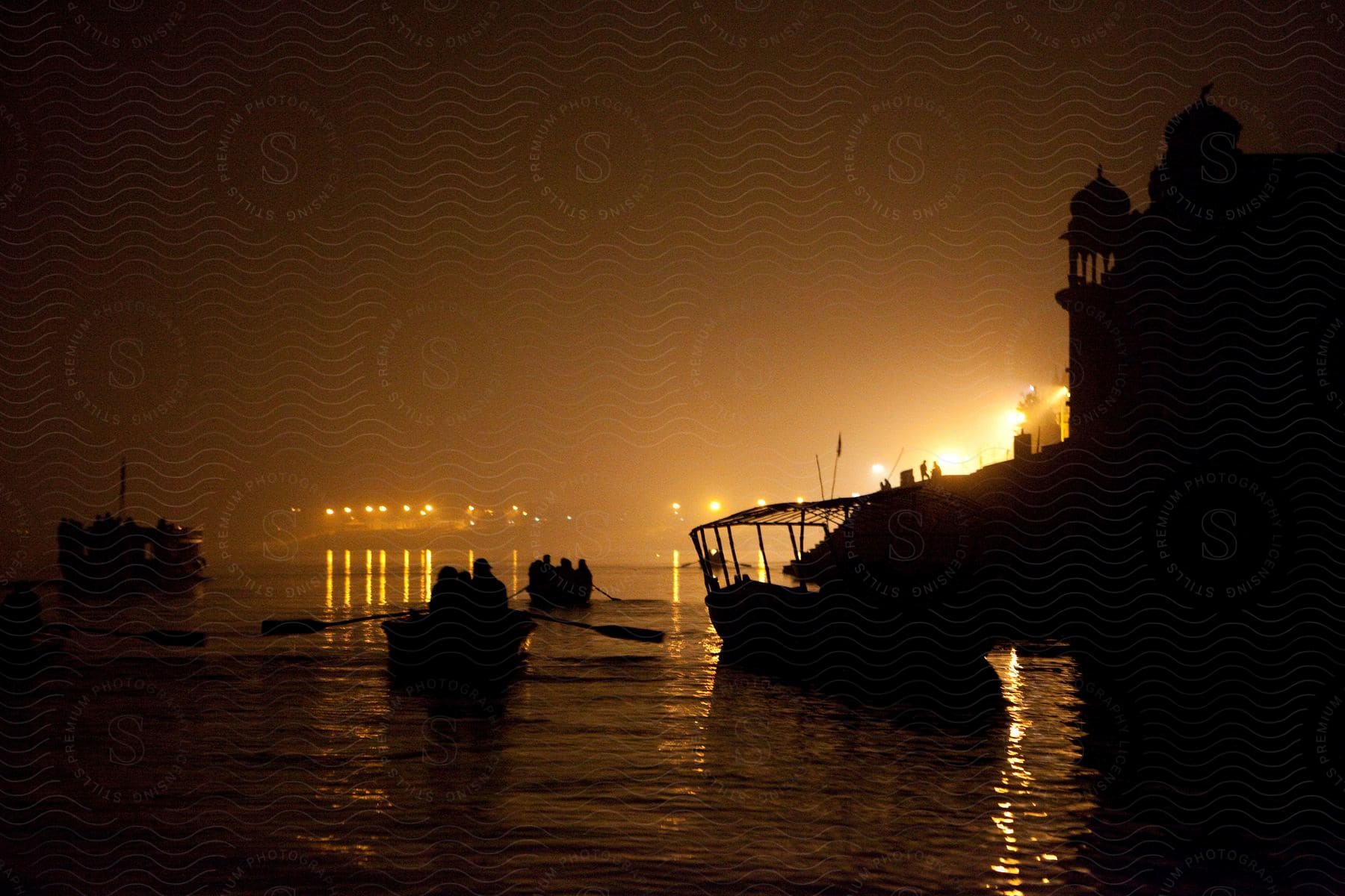 Rowboats with people inside passing next to the coast of a city at night