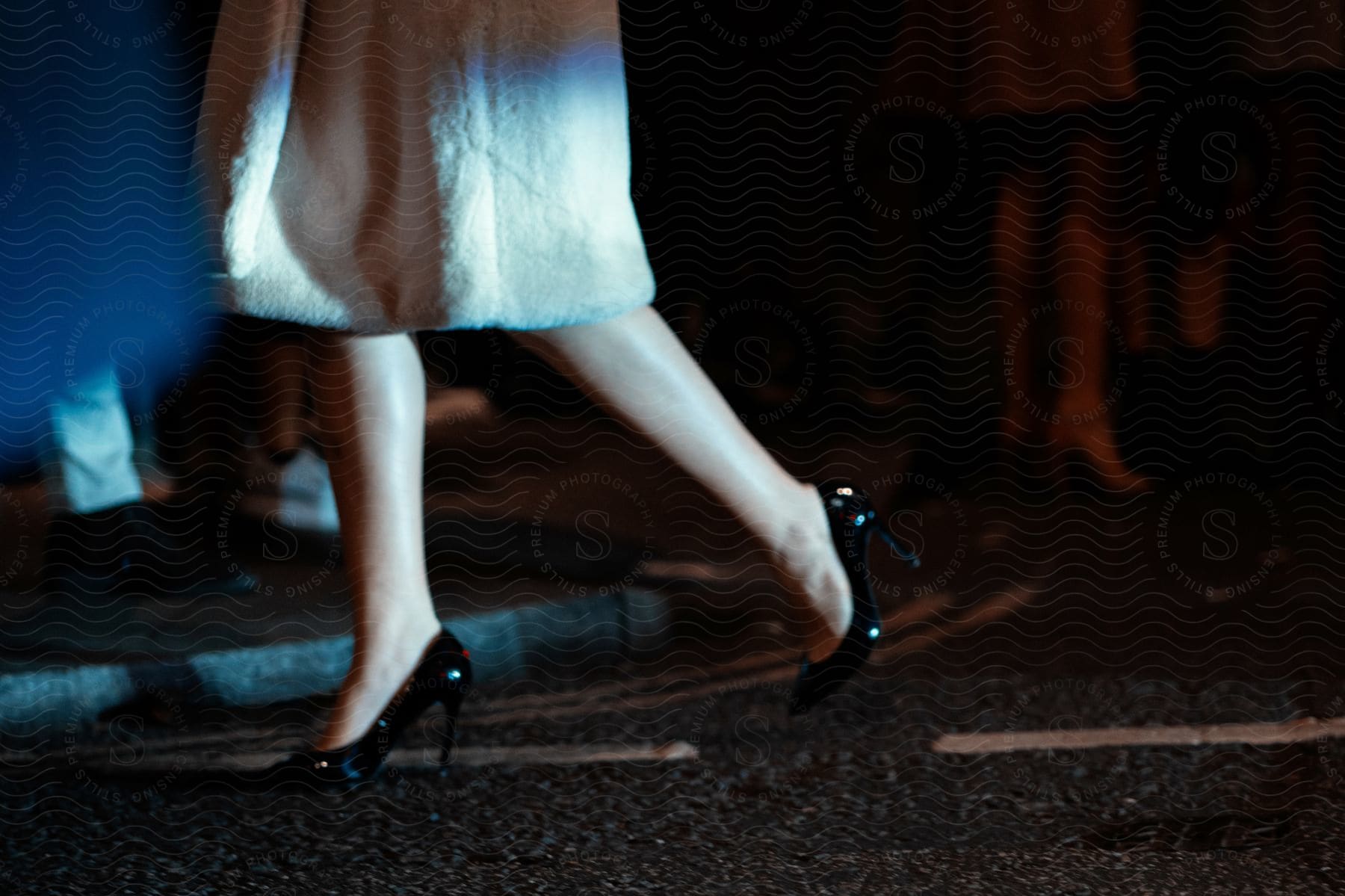 A woman walks on a road near a sidewalk at night in black high heels