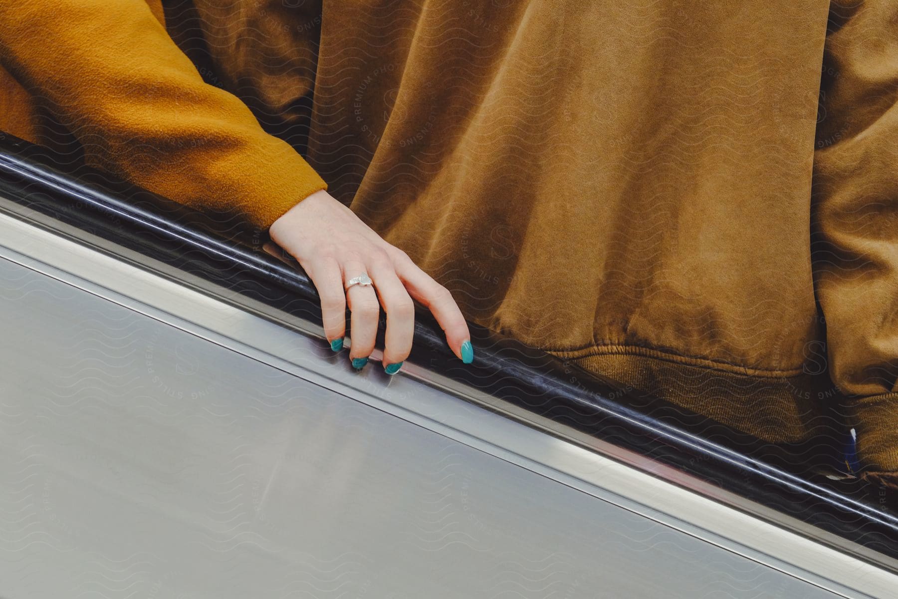 A womans hand with aqua painted nails holds the railing of an escalator