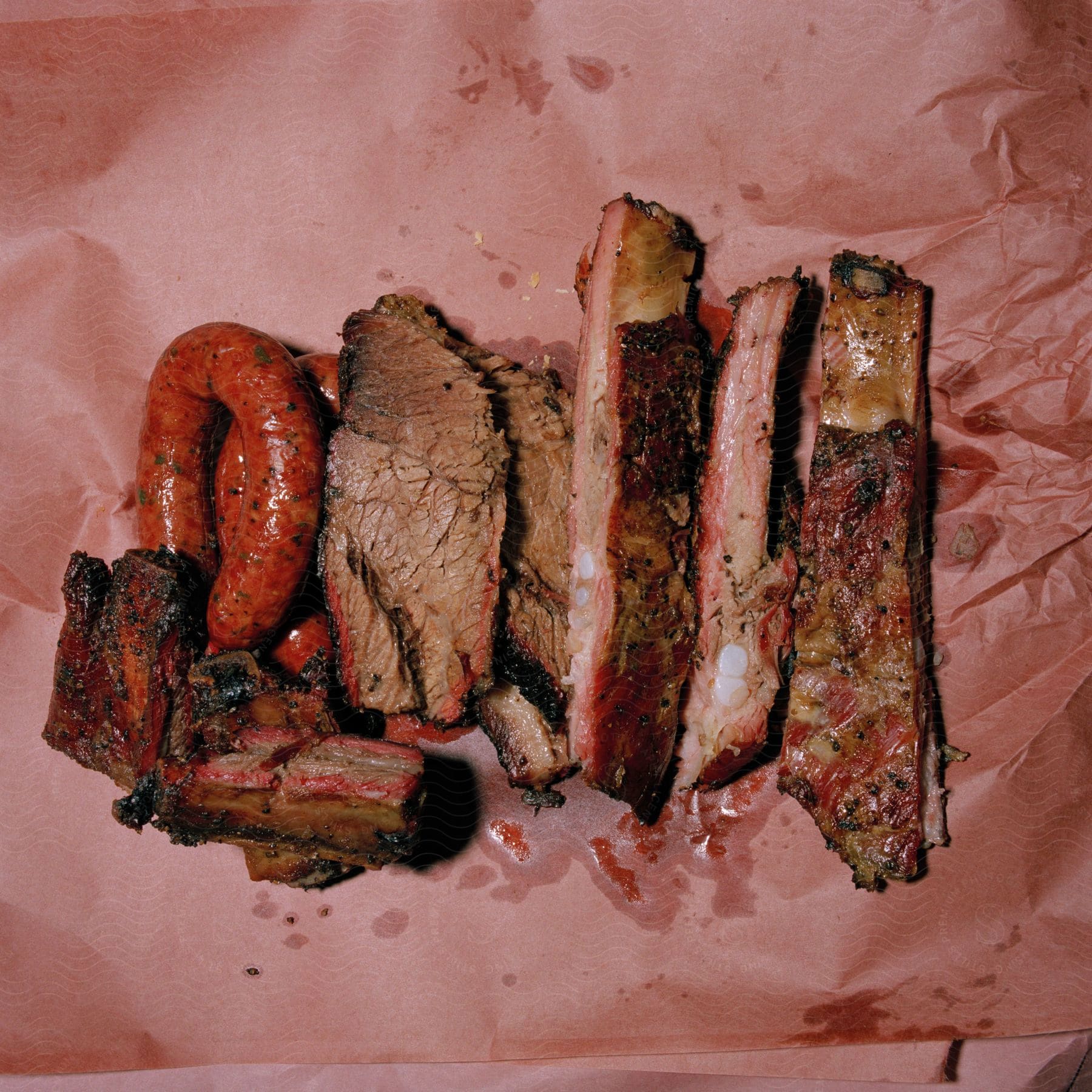 Ribs sausage and other meat are shown on pink paper
