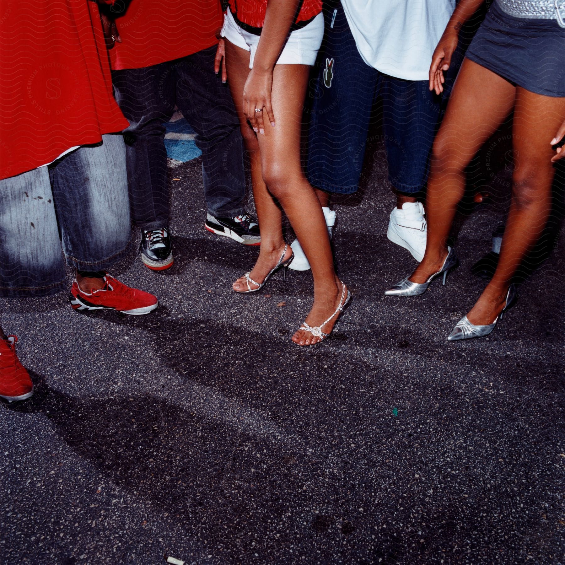 Five pairs of legs standing on a road two pairs from women in miniskirts and three from men in baggy shorts or pants