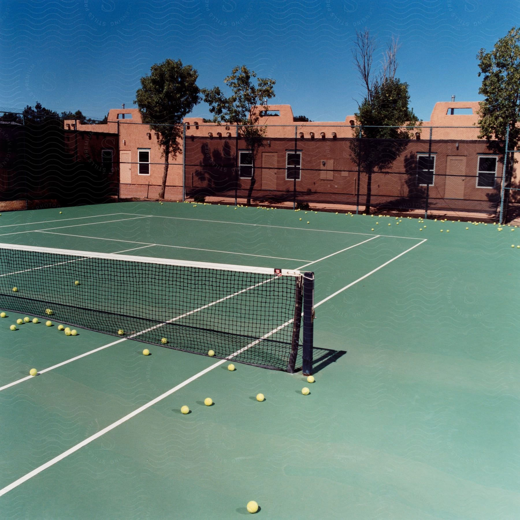 A tennis court with scattered tennis balls on the ground on a sunny day