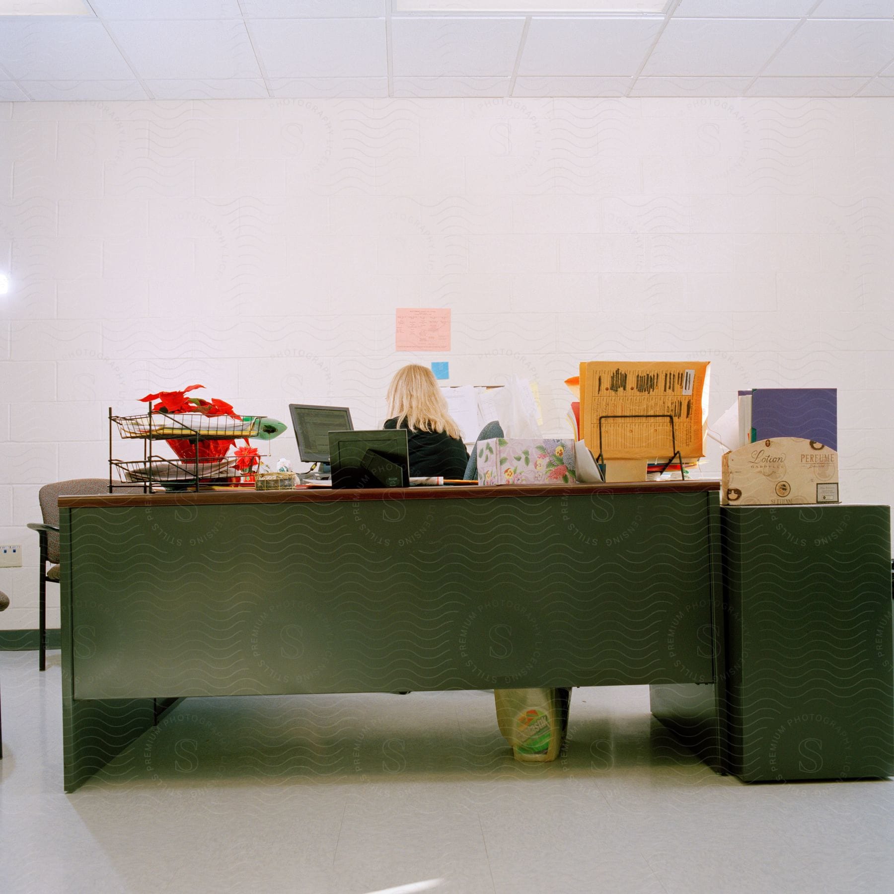 A blonde woman is working at a desk in an office operating a computer