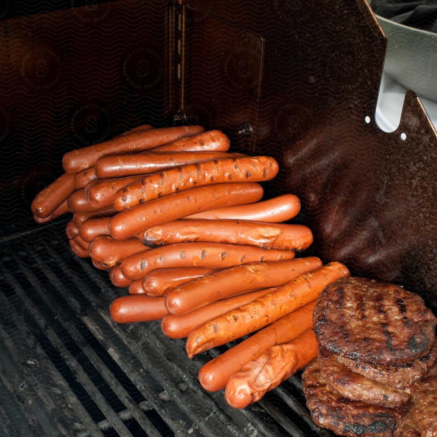 Stock photo of a mountain of sausages and burgers being cooked on a grill