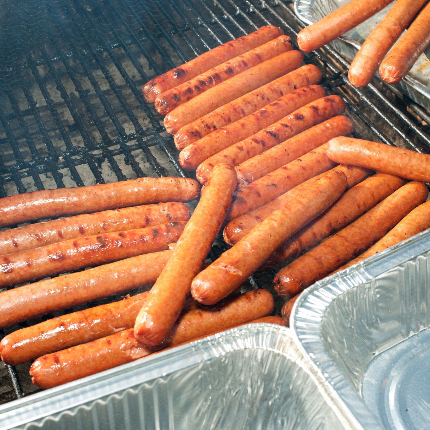 Several sausages being grilled ready to be packaged in aluminum containers