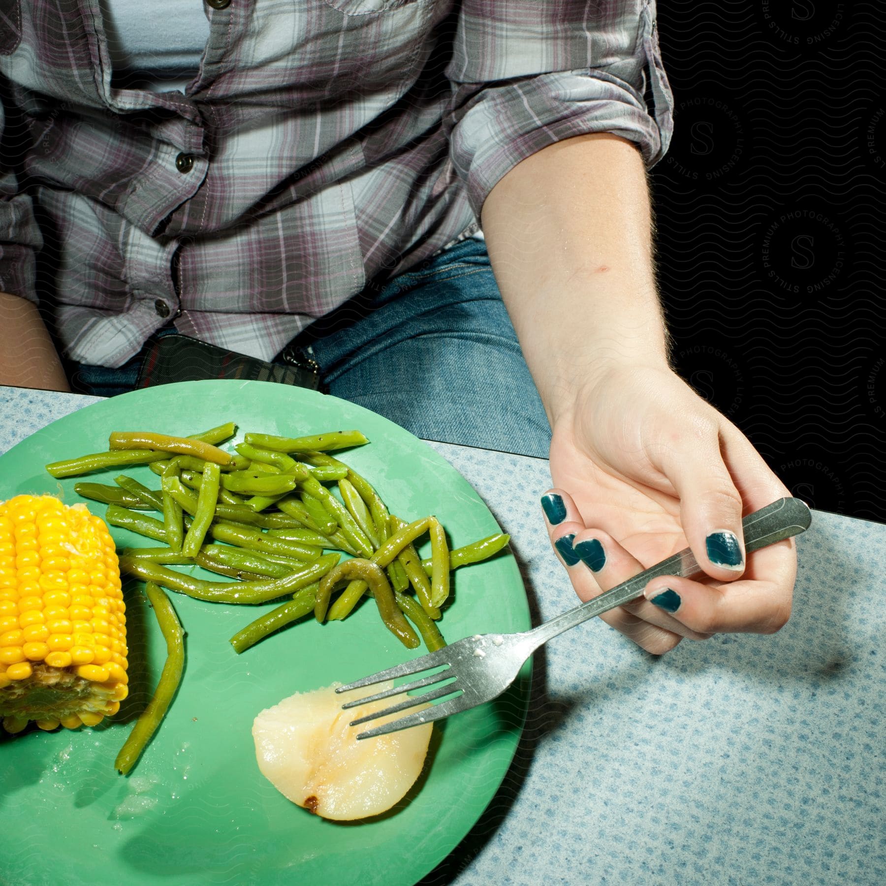 A person is sitting at a table and eating a plate of vegetables with okra and corn