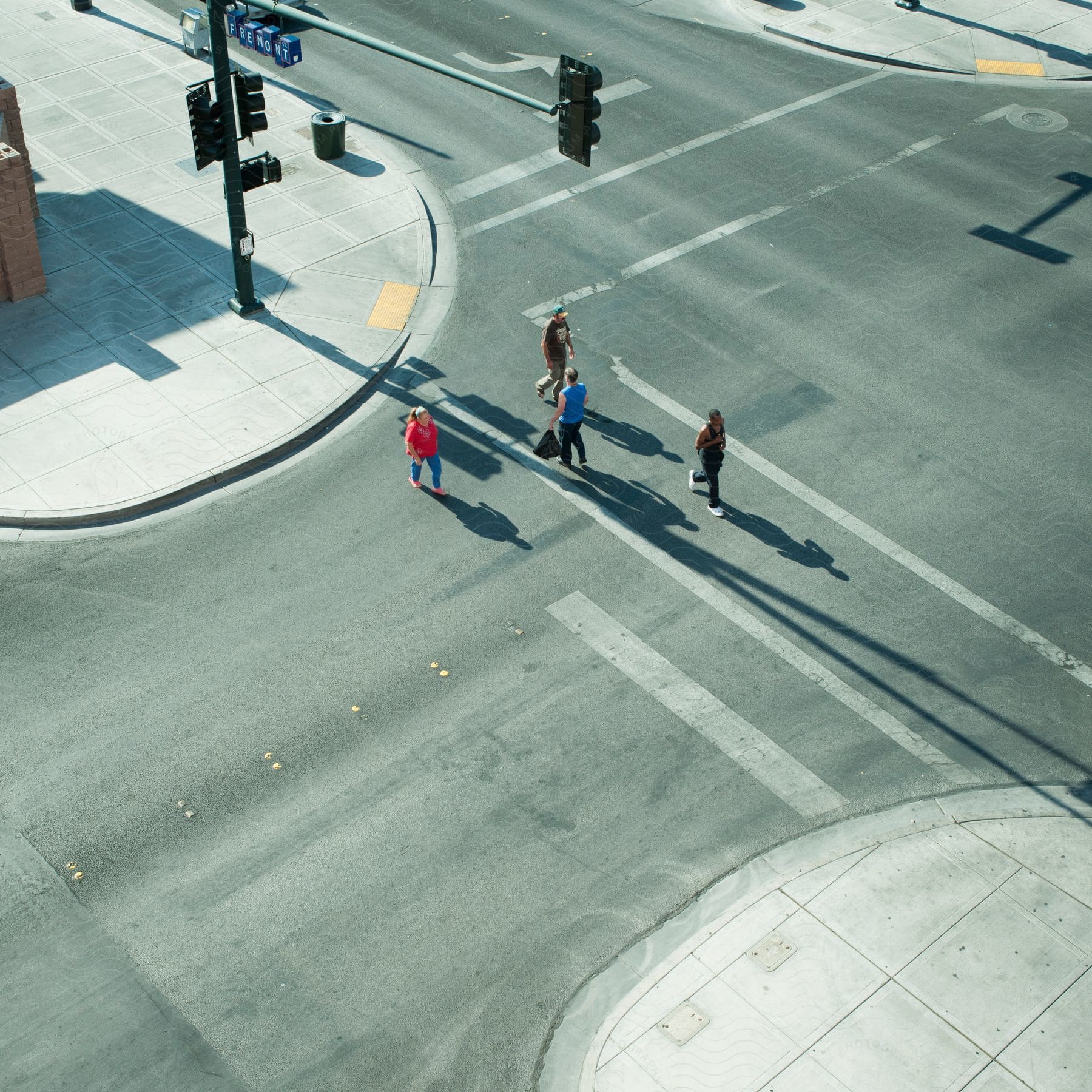 A group of people crossing a paved street at an intersection with traffic lights in a city