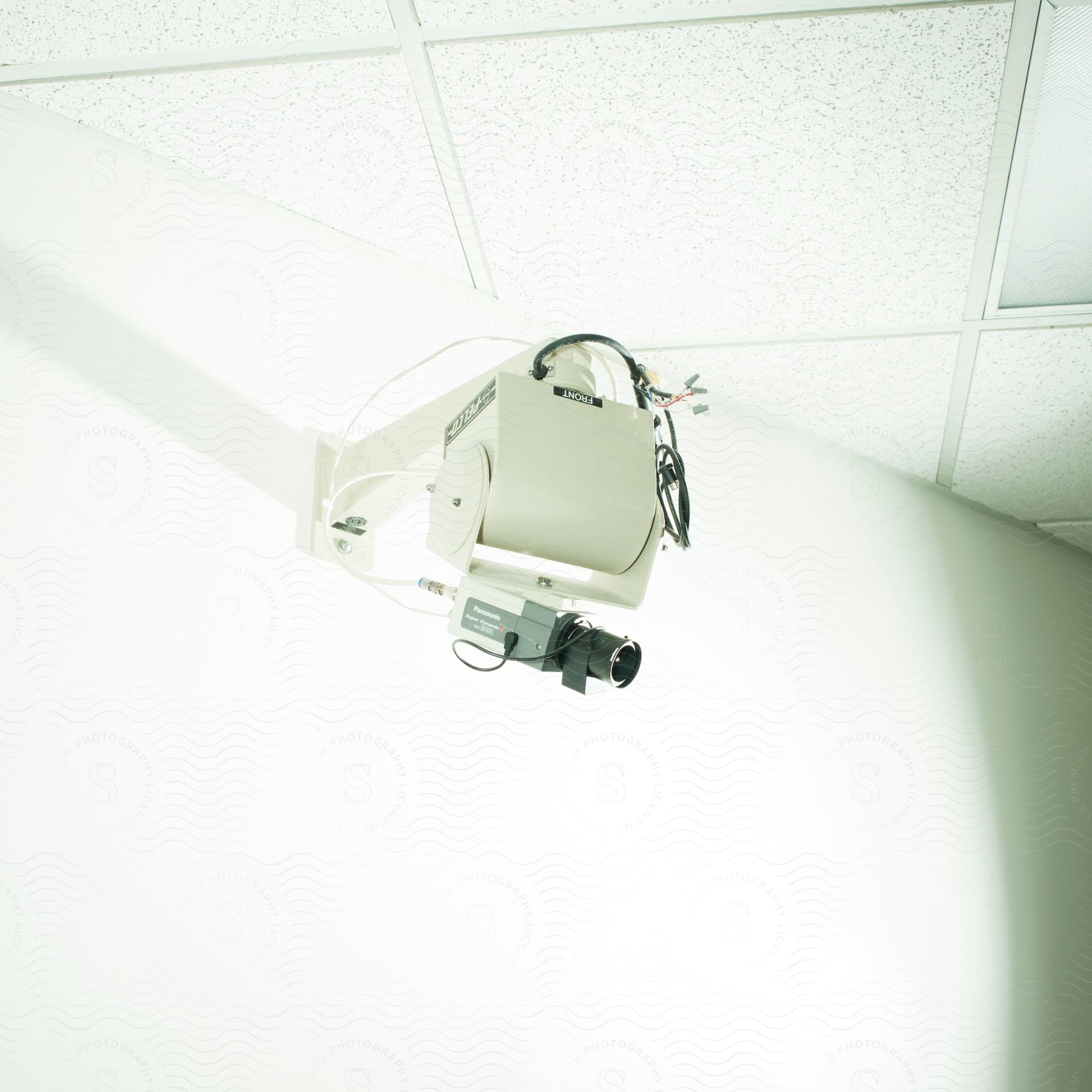 A surveillance camera positioned high on a wall under a tiled ceiling