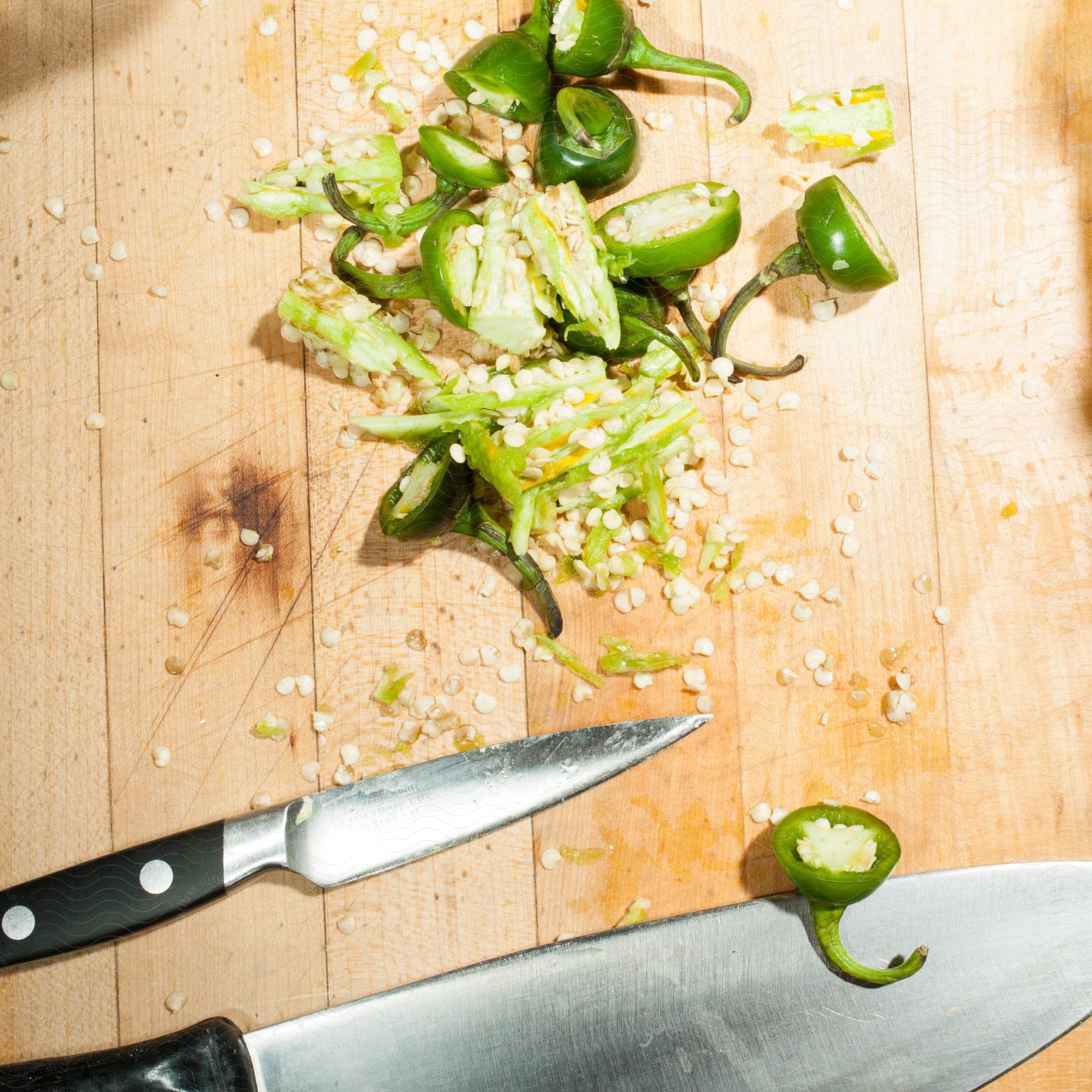 Stock photo of a bunch of sliced jalapeno peppers on a table with a couple of knives next to it