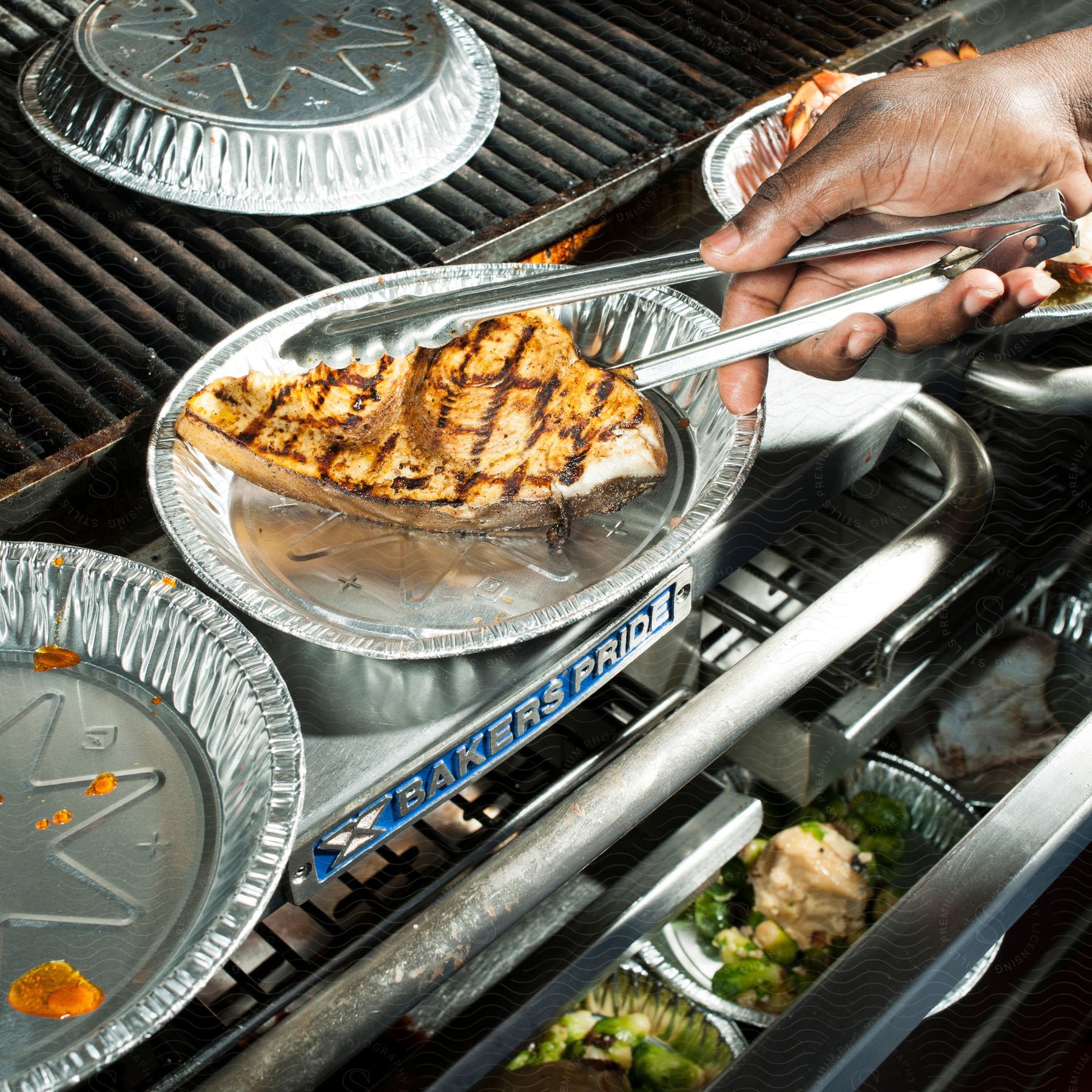 Stock photo of a person uses tongs to handle meat on a barbecue grill