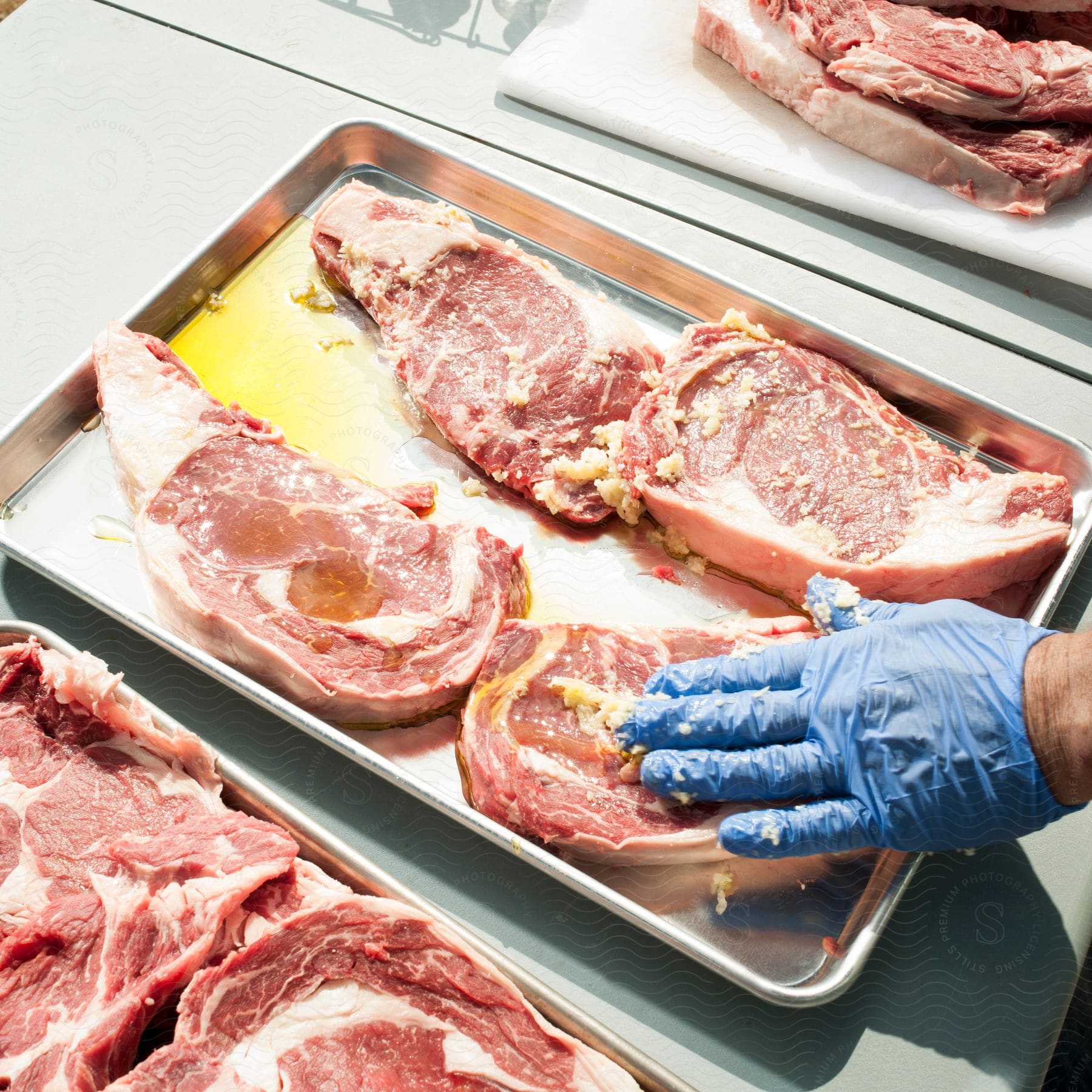 A person seasons a tray of steaks